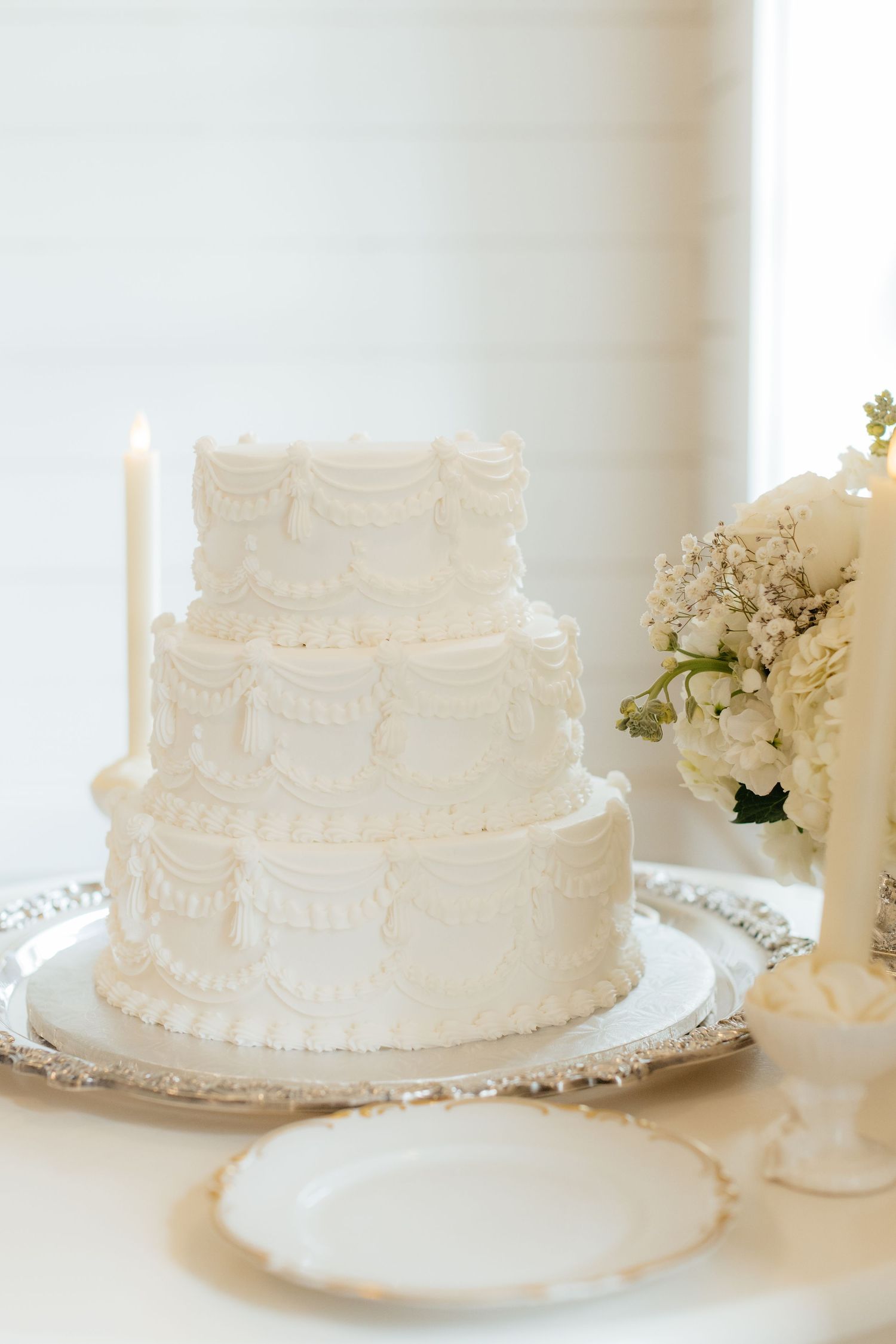 Classic white wedding cake with delicate piped details displayed on a silver platter.