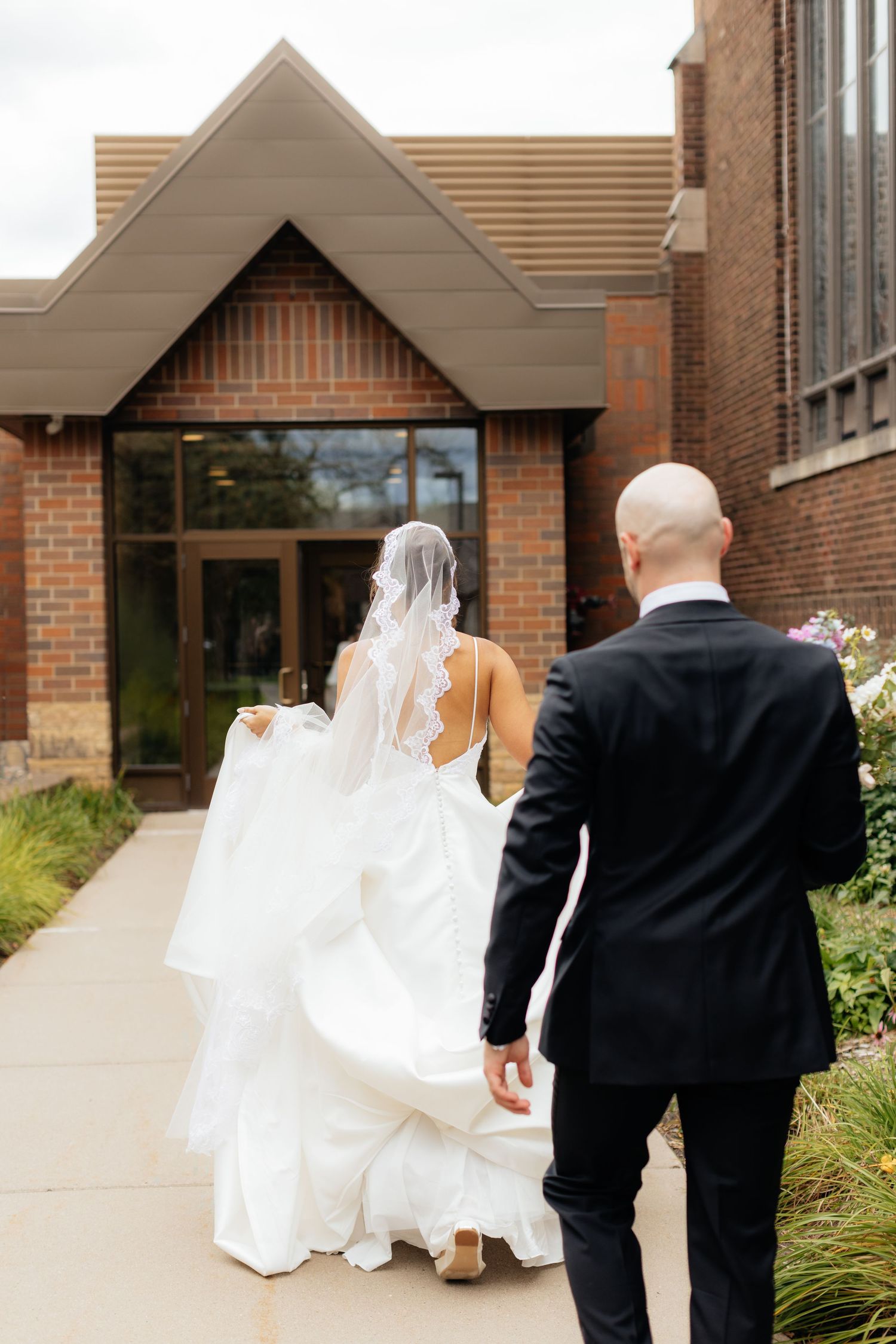 Wedding couple walking together outside a brick church building.