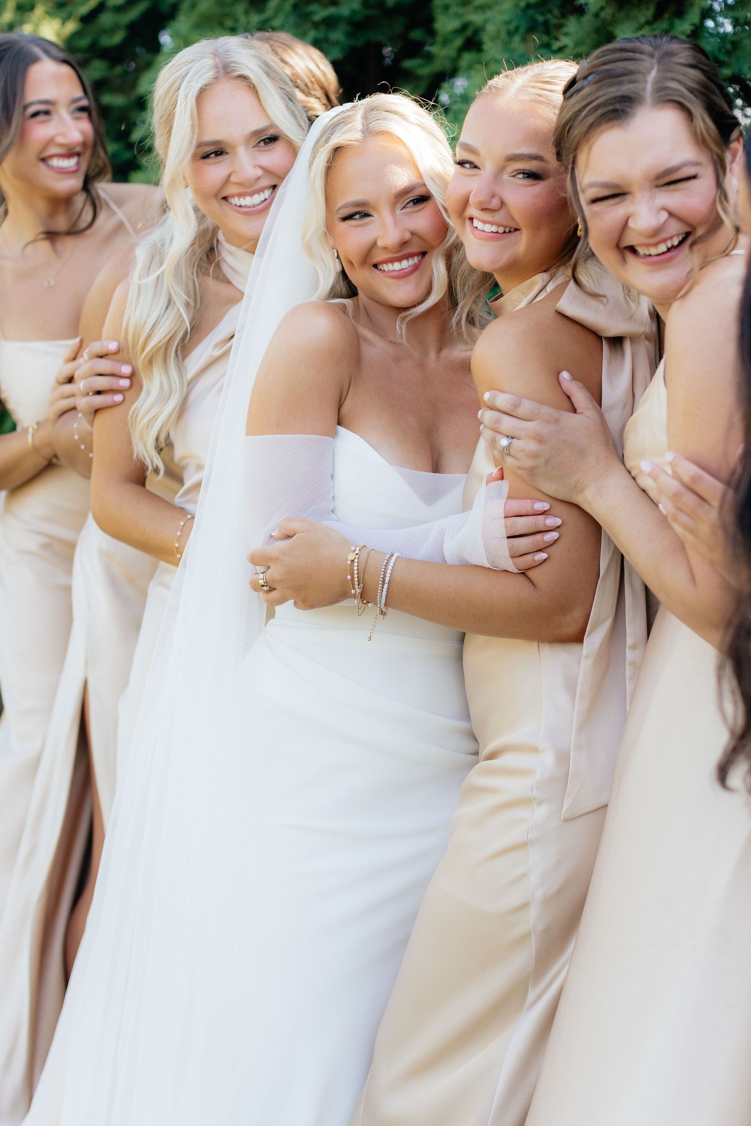 Bridal party in cream and white dresses share joyful moment together.