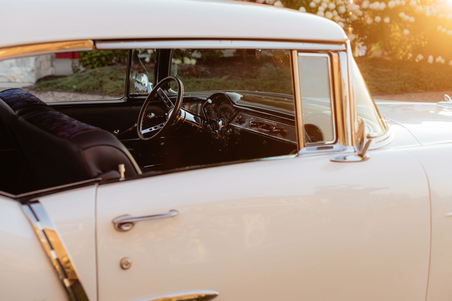 Interior view of a classic cream-colored vintage car dashboard and steering wheel at sunset.