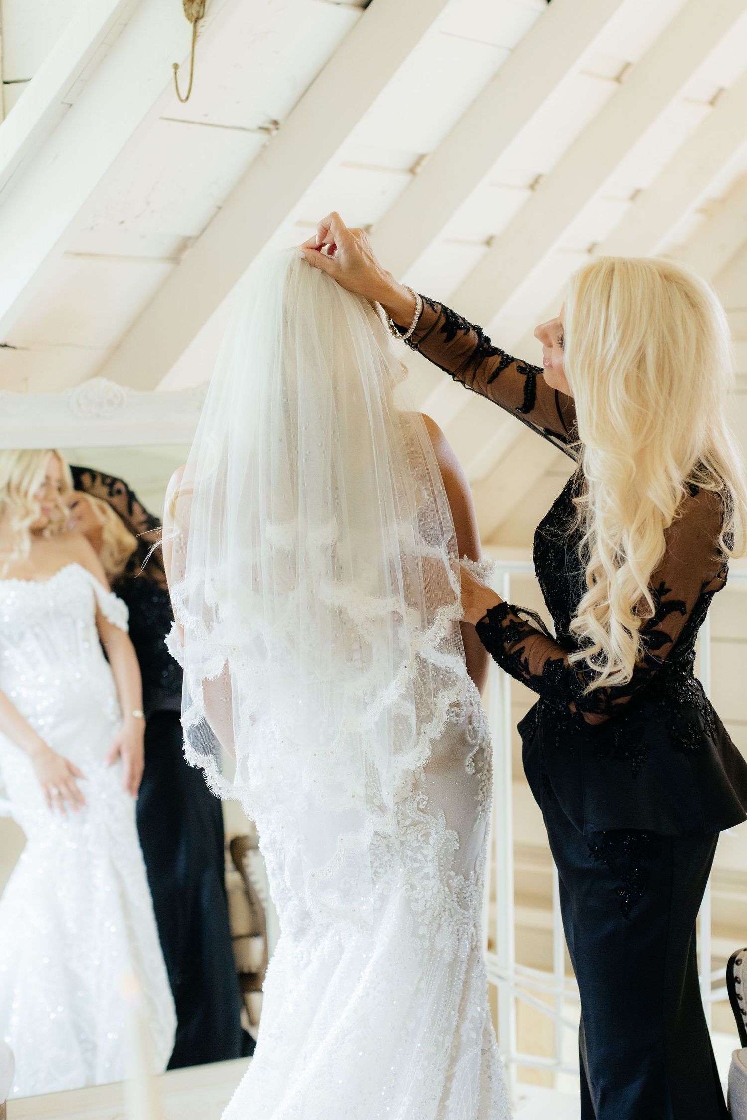Wedding veil being carefully adjusted on a white lace bridal gown.