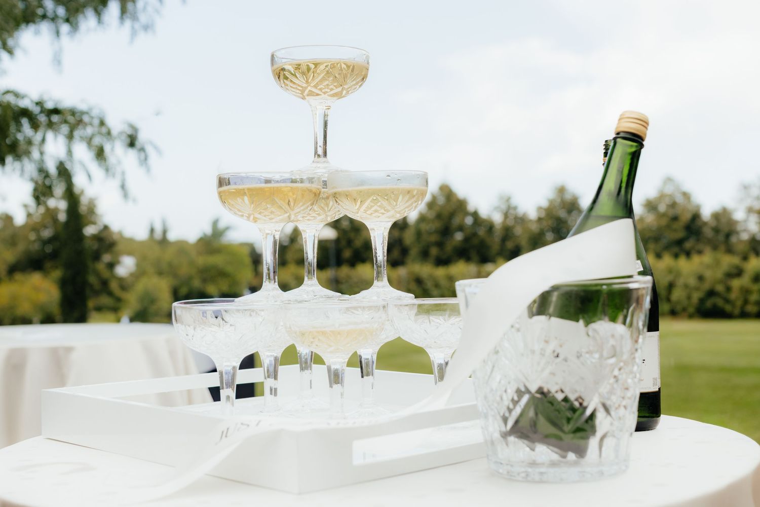 Champagne tower being filled with sparkling wine at an outdoor wedding reception.