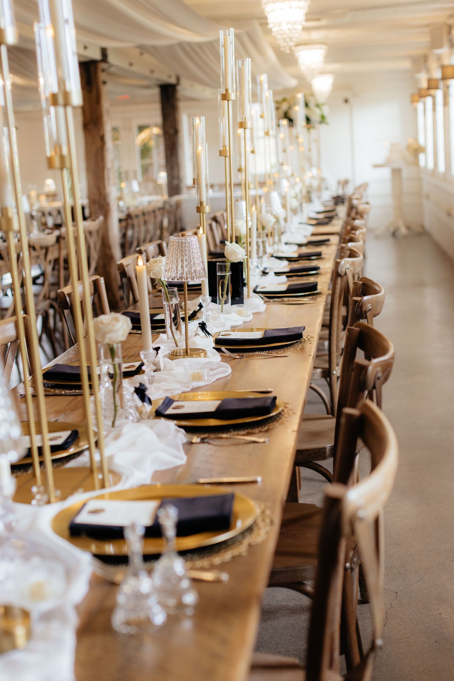Elegant wedding reception table settings with gold candles and black charger plates in a grand ballroom.