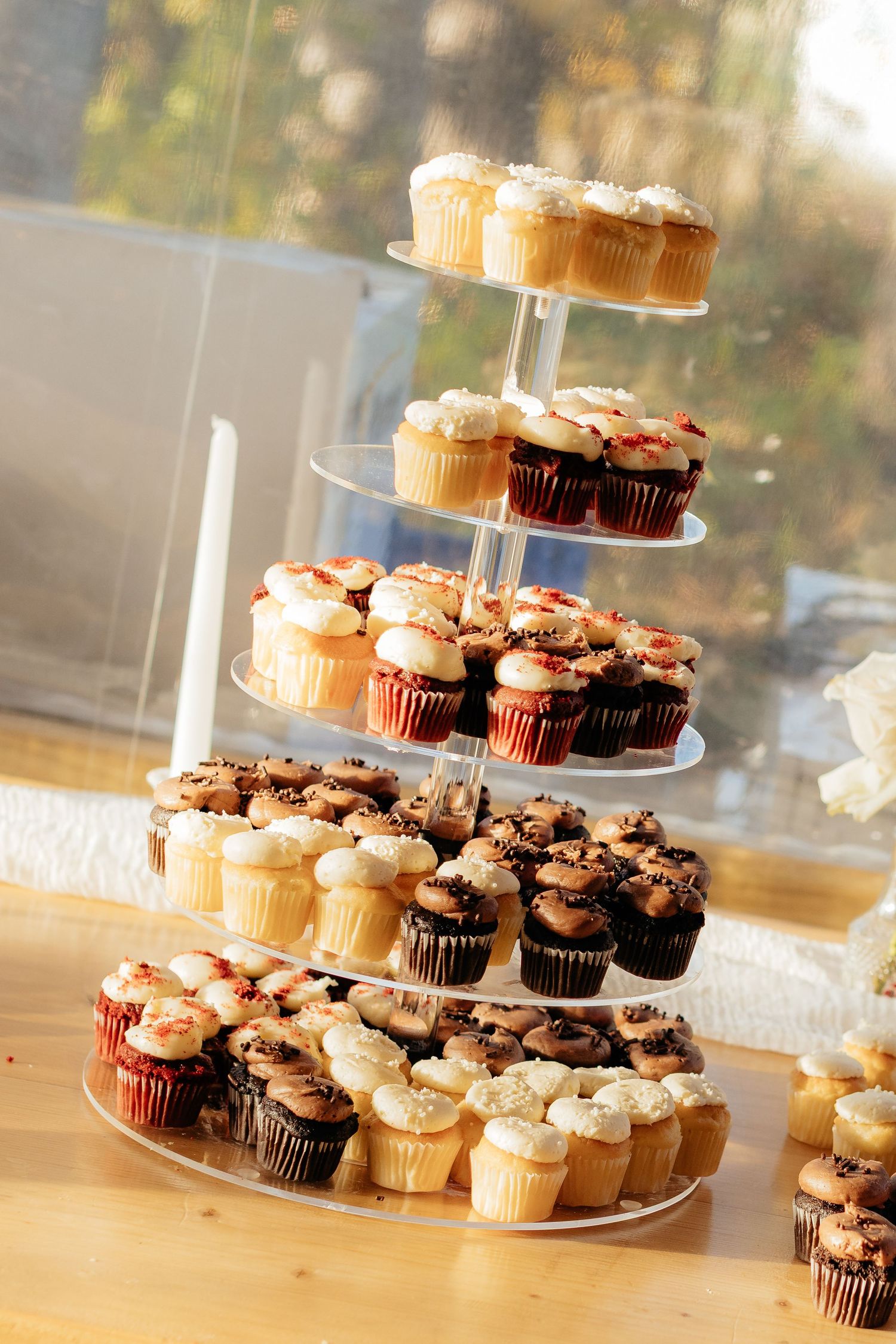 Tiered display of chocolate and vanilla cupcakes with frosting arranged on clear cake stands at a reception.