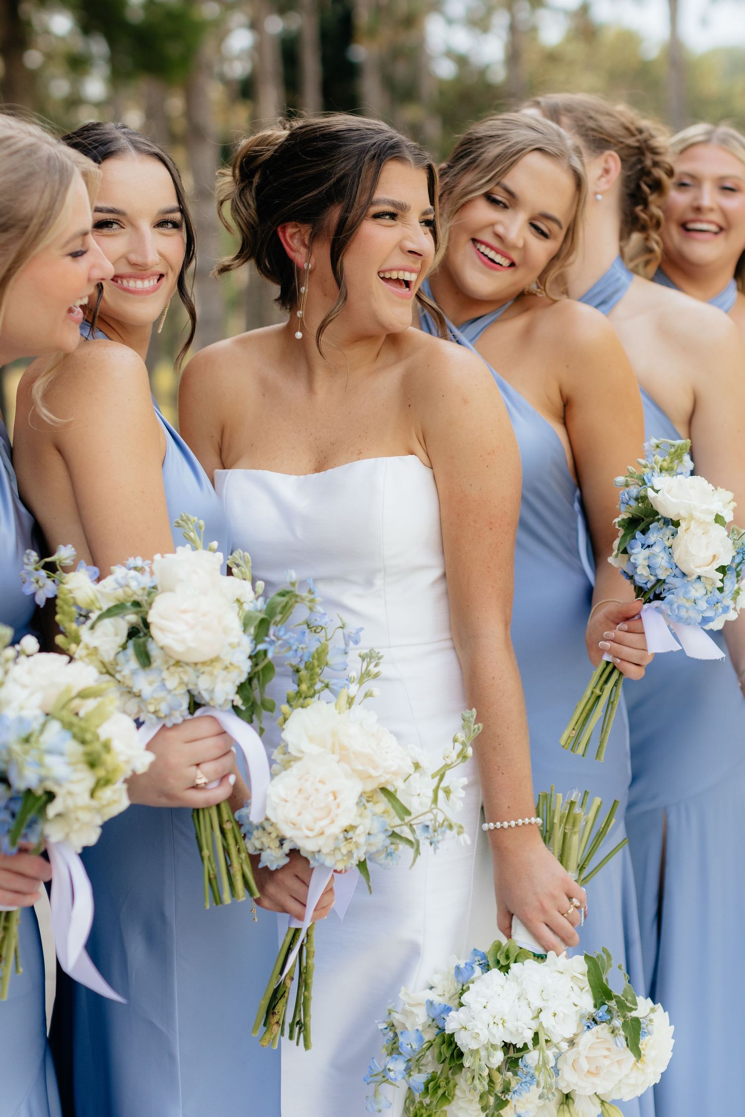 Bridesmaids in light blue dresses hold white bouquets in outdoor wedding photo.