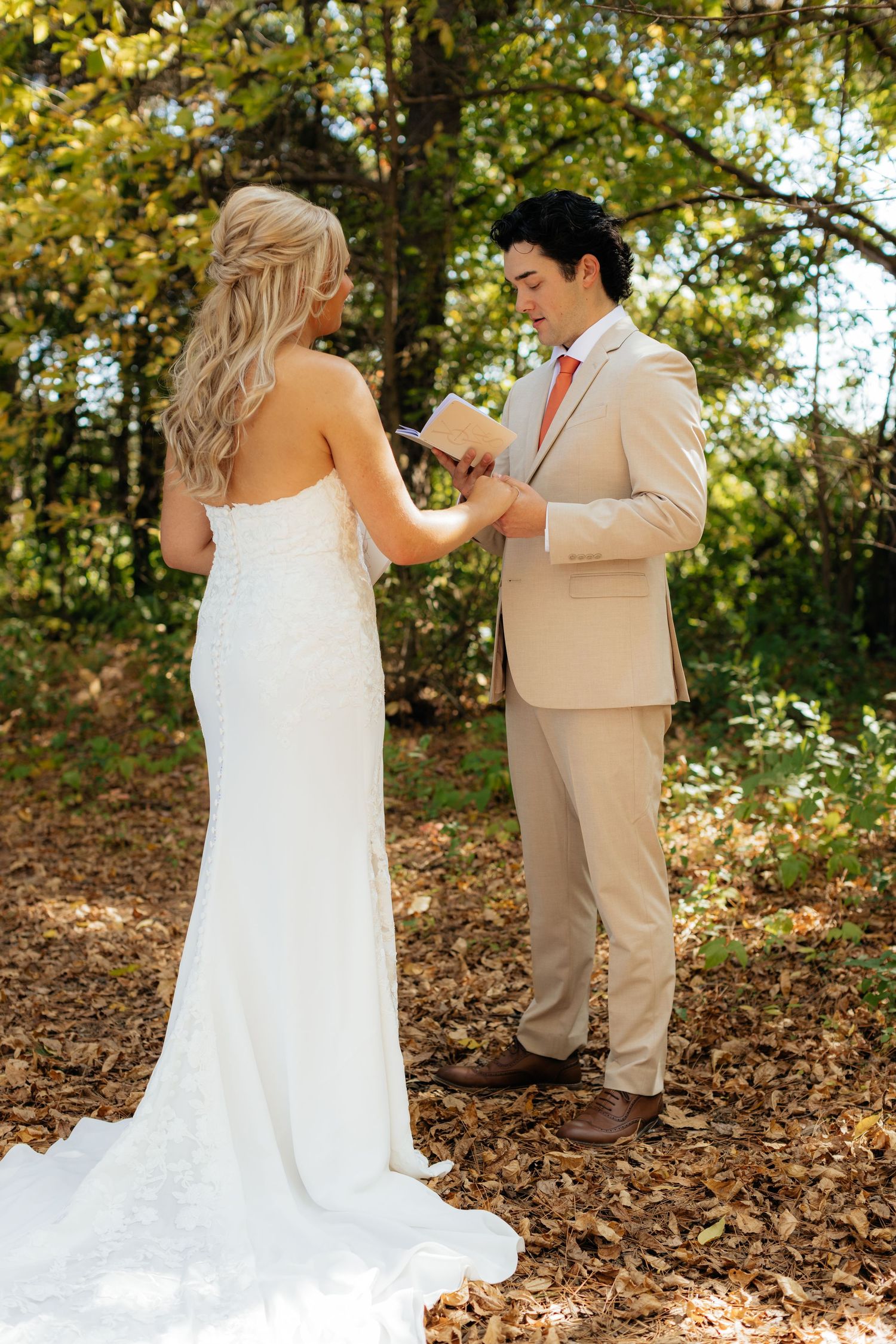 A couple shares their first look moment in a wooded area with autumn leaves on the ground.