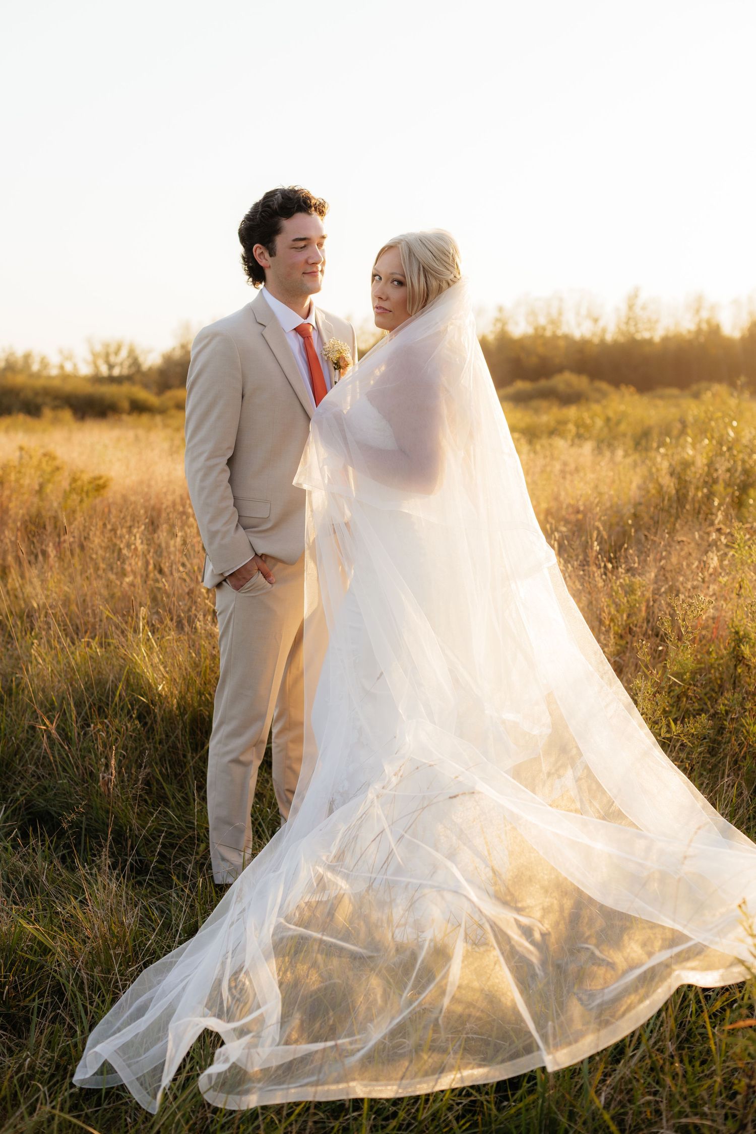 Bride's veil flows dramatically in the wind during sunset wedding photoshoot.