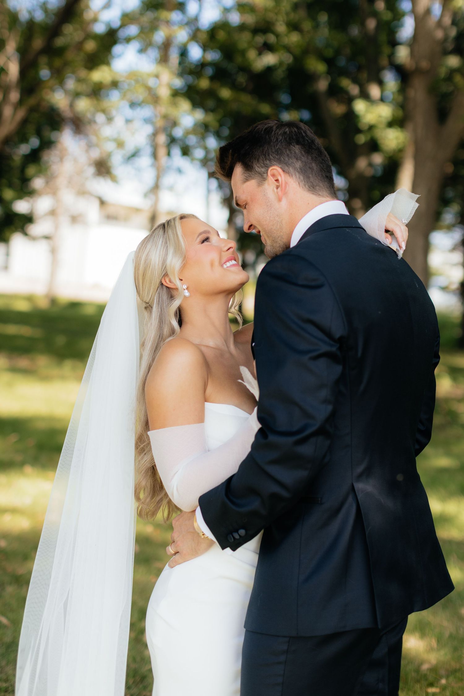 Romantic wedding couple shares intimate moment outdoors with sunlit trees in background.