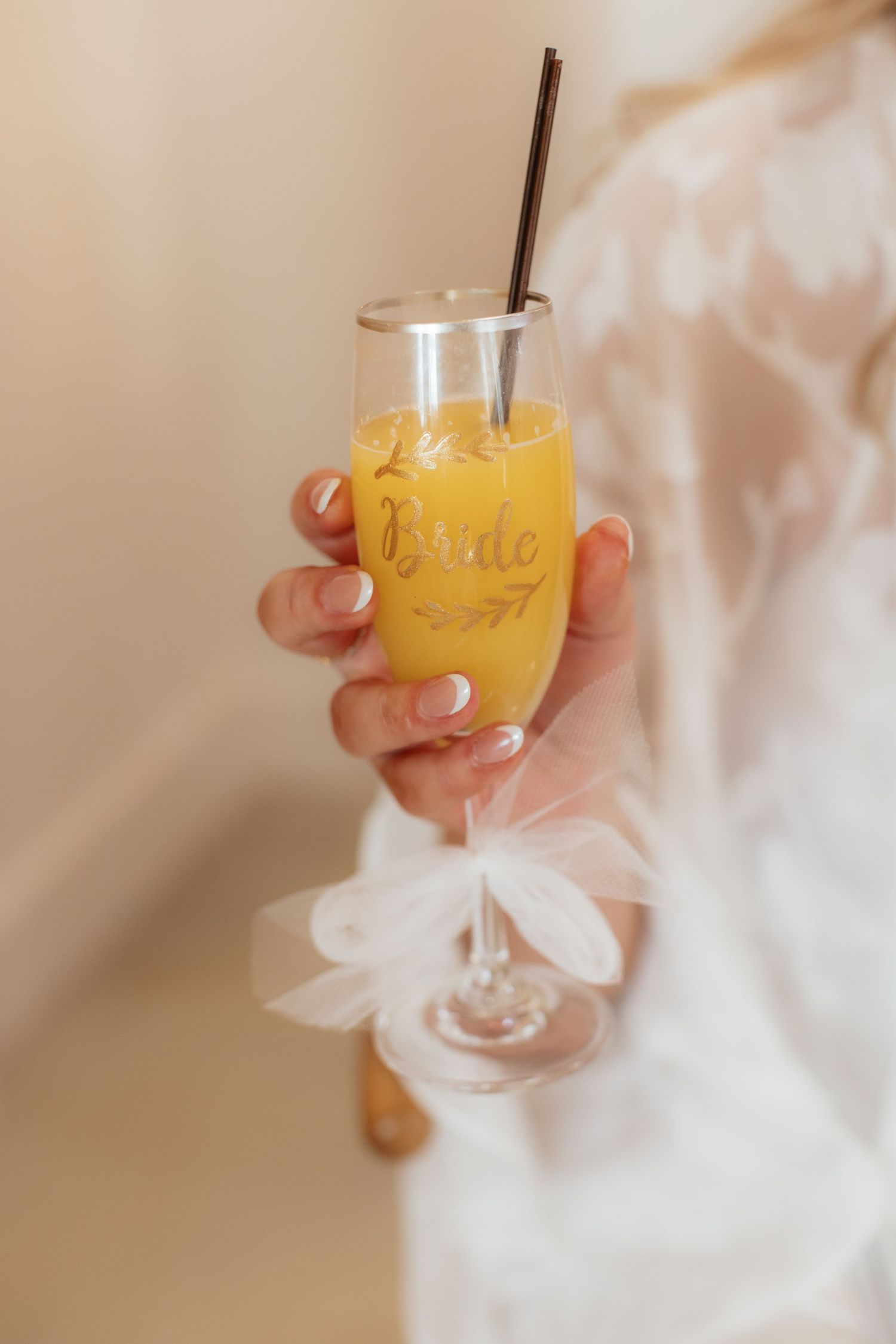 Orange signature cocktail in a stemmed glass with bride's white dress in background.