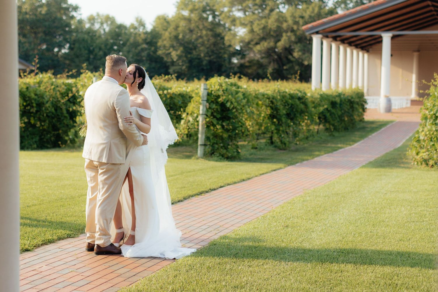 Newlyweds embrace on a brick pathway surrounded by lush gardens.