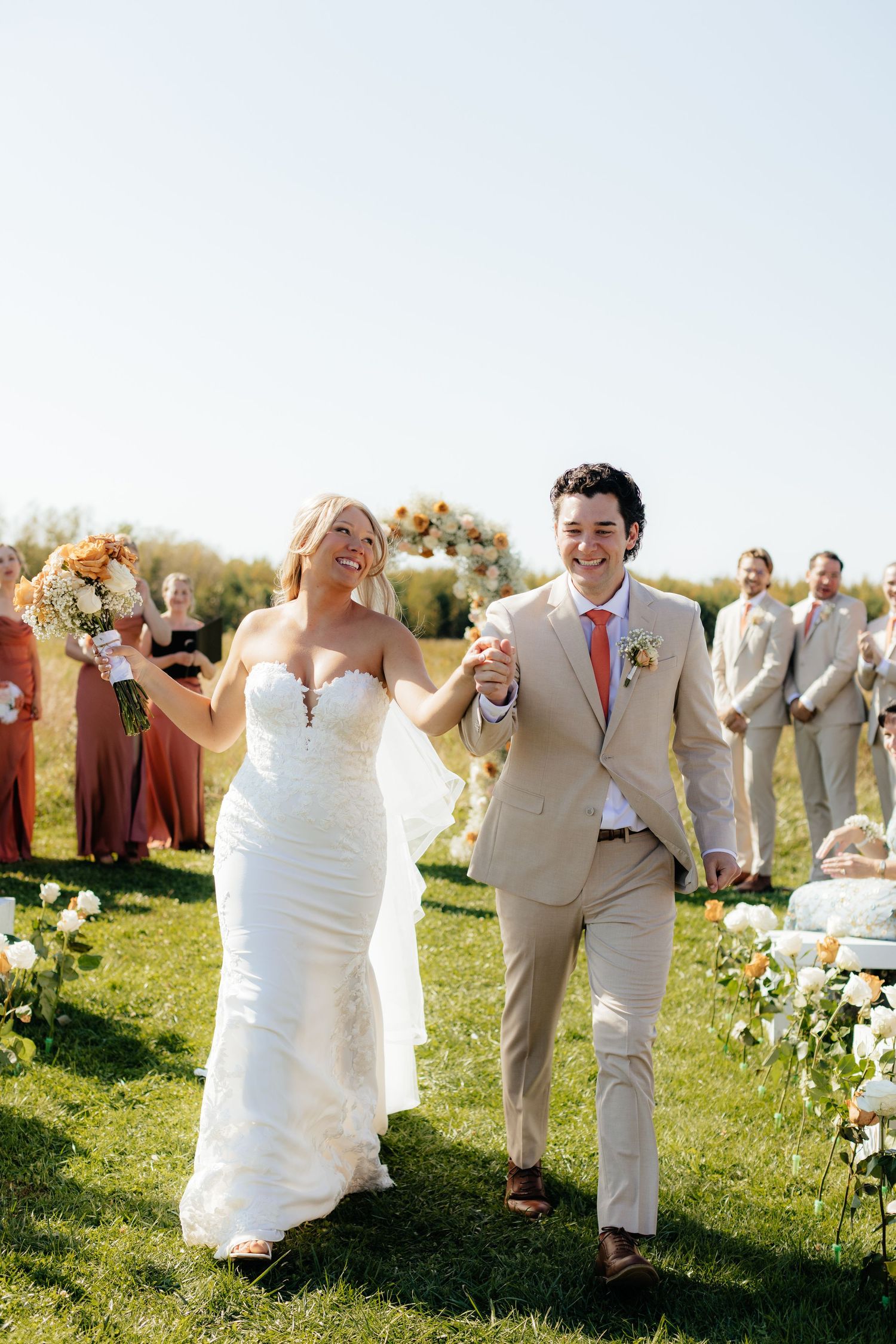 Wedding party celebrates with joyful dance moves in a grassy field during golden hour.