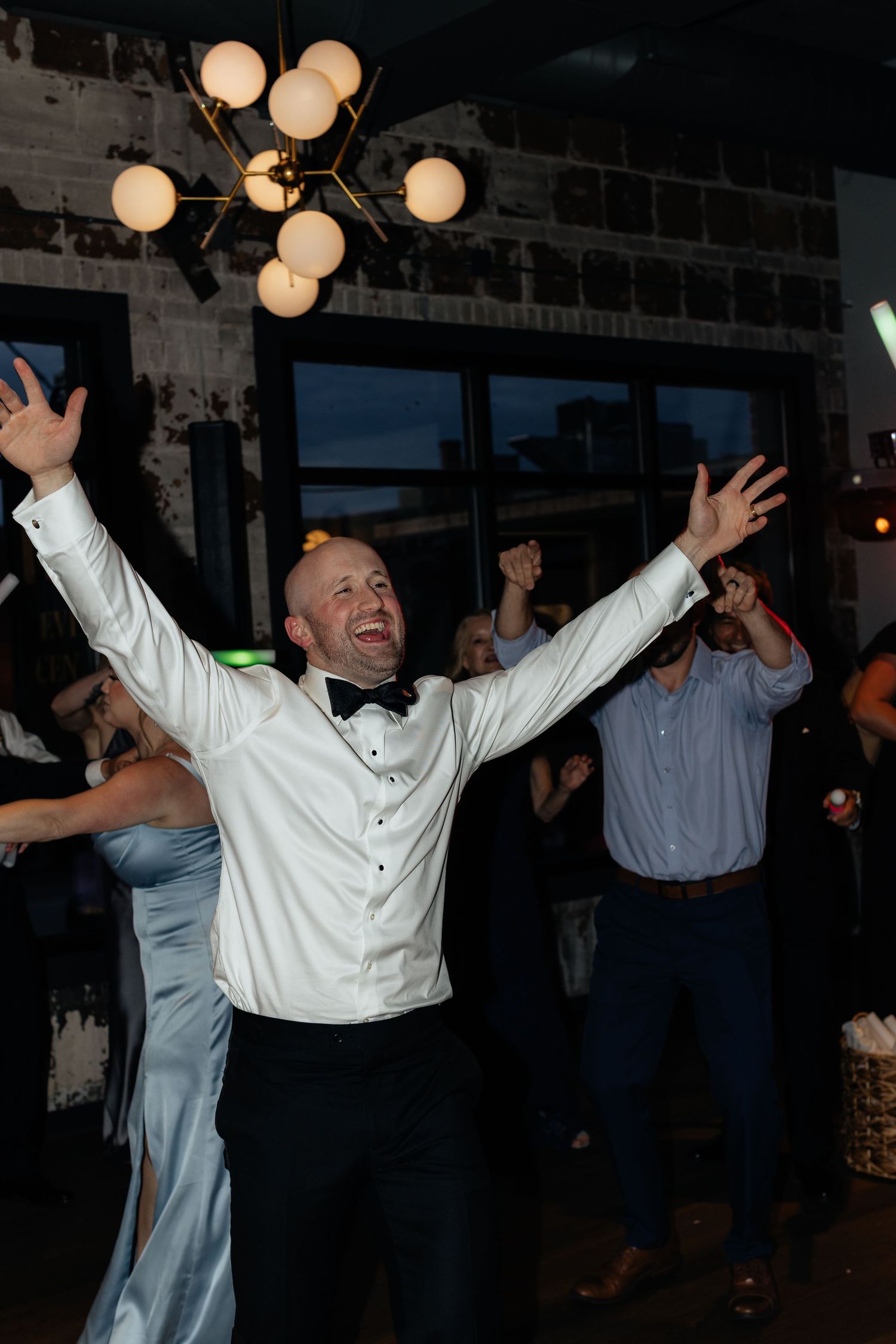 A person in white celebrates enthusiastically on a dance floor with arms raised.