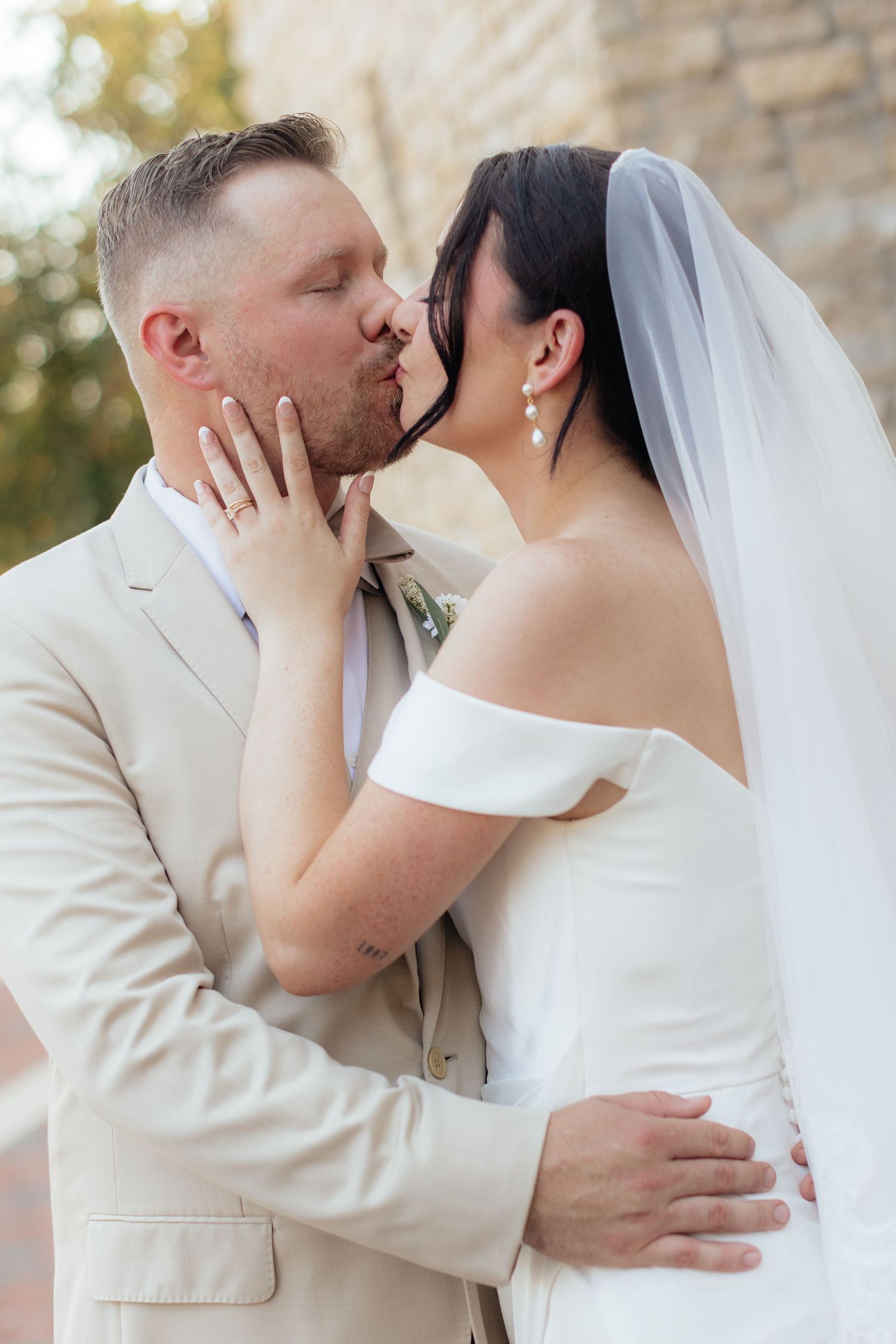 A romantic wedding kiss between newlyweds, with the bride in white and groom in beige suit.