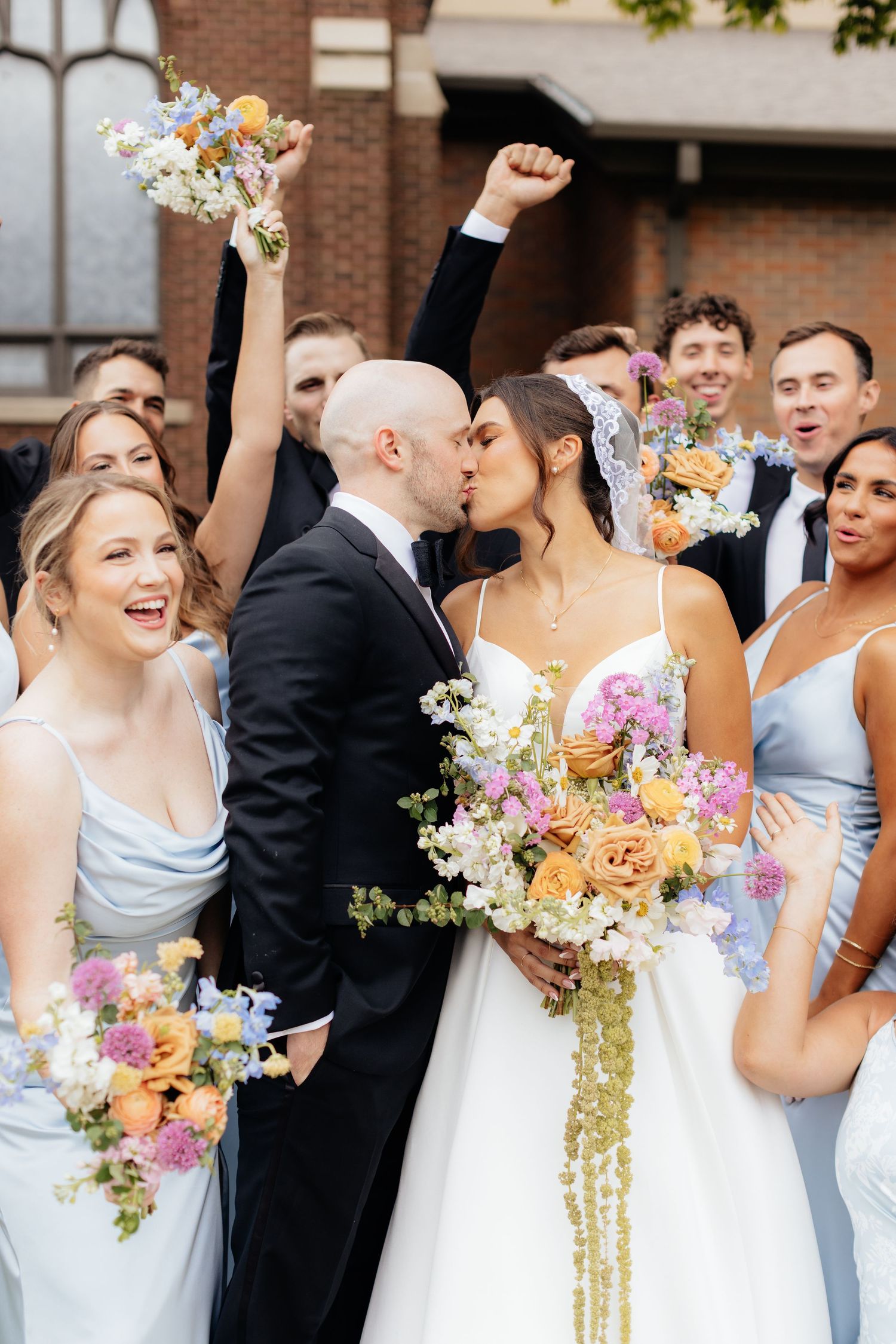 Joyful wedding party celebrates with colorful bouquets during outdoor ceremony.