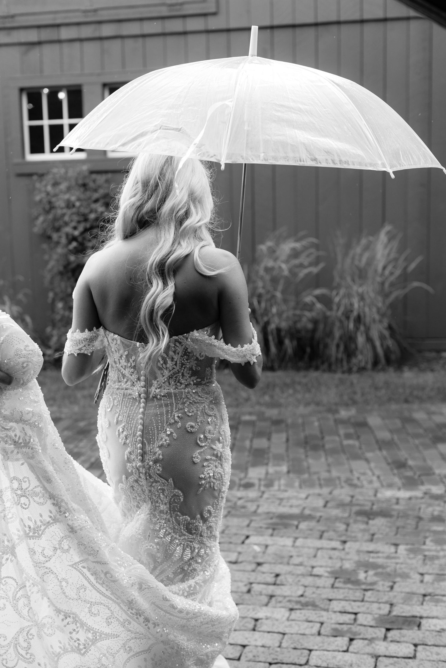 Elegant lace wedding dress detail with delicate white parasol against rustic barn backdrop.