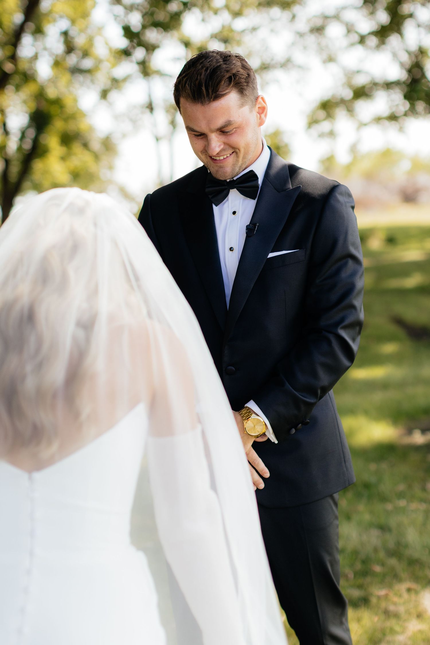 Groom watches bride's veil flow in the breeze during outdoor photo session.