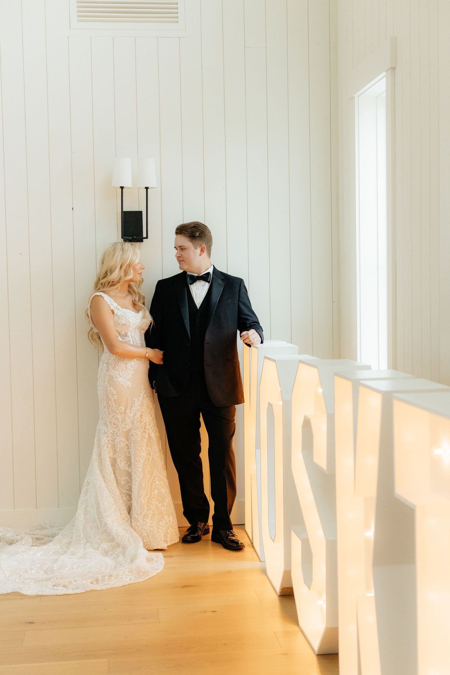 Wedding couple poses in bright white interior room with backlit windows.