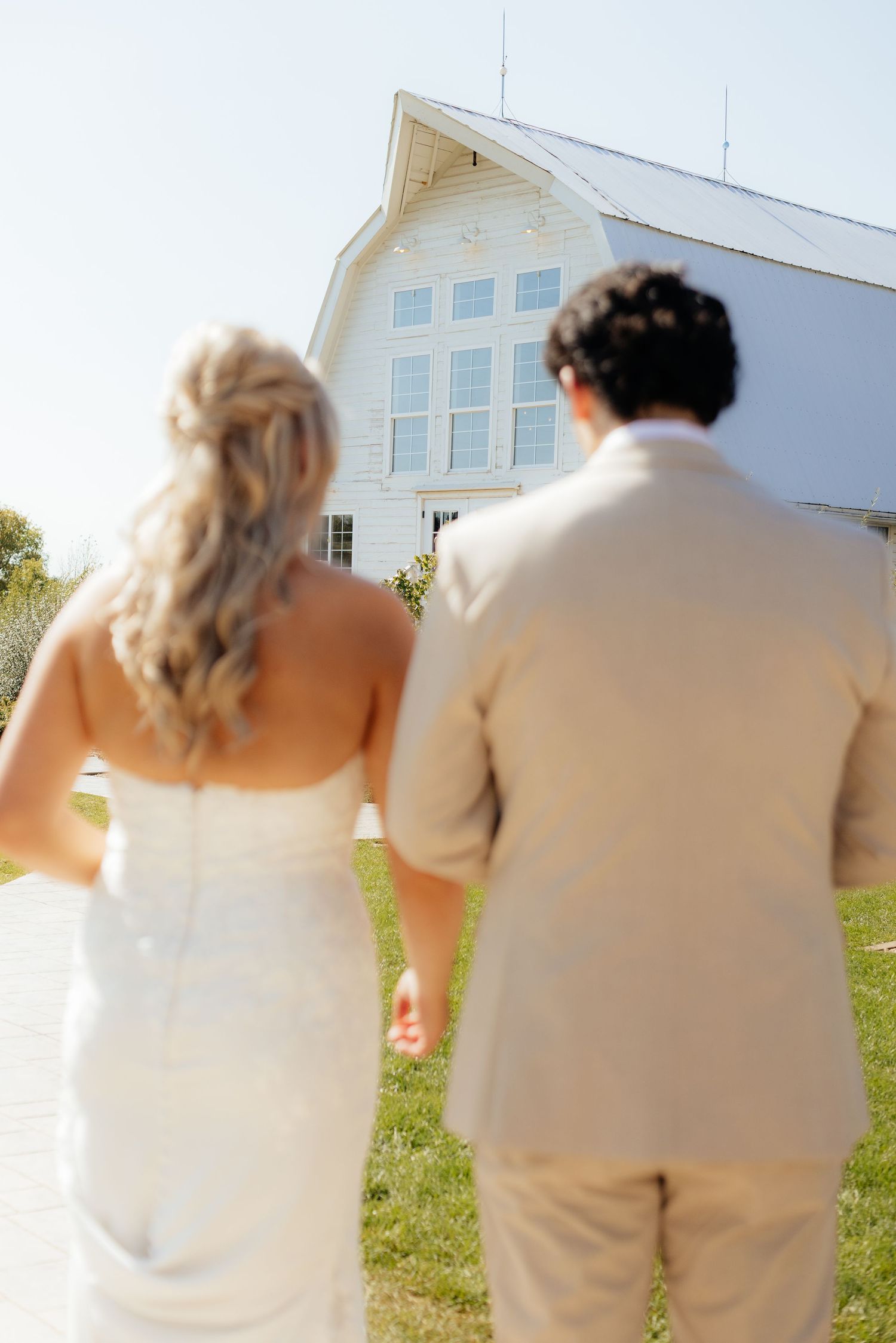 Wedding couple photographed from behind against white building exterior.