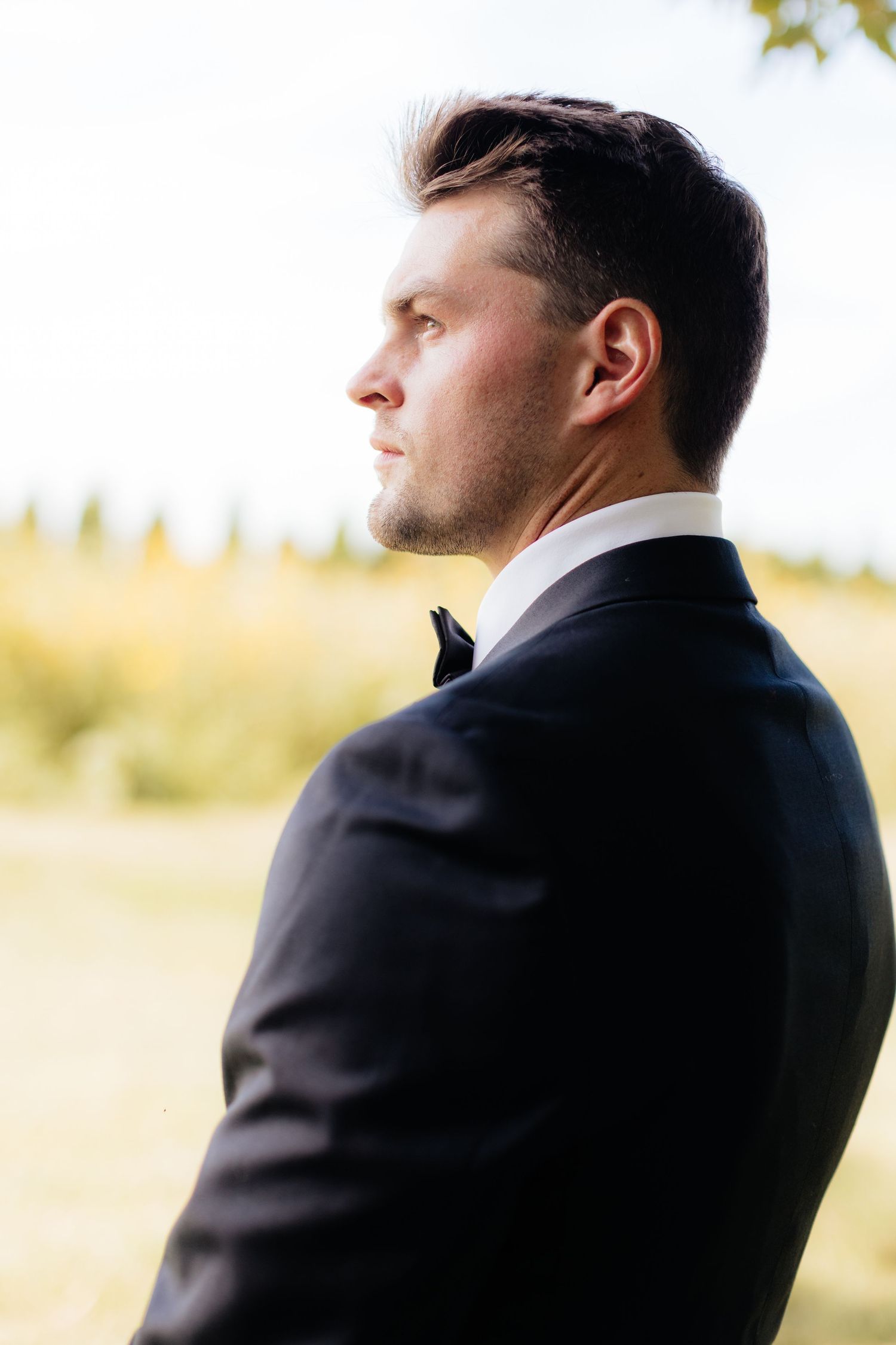 Groom in black tuxedo gazes thoughtfully into the distance.