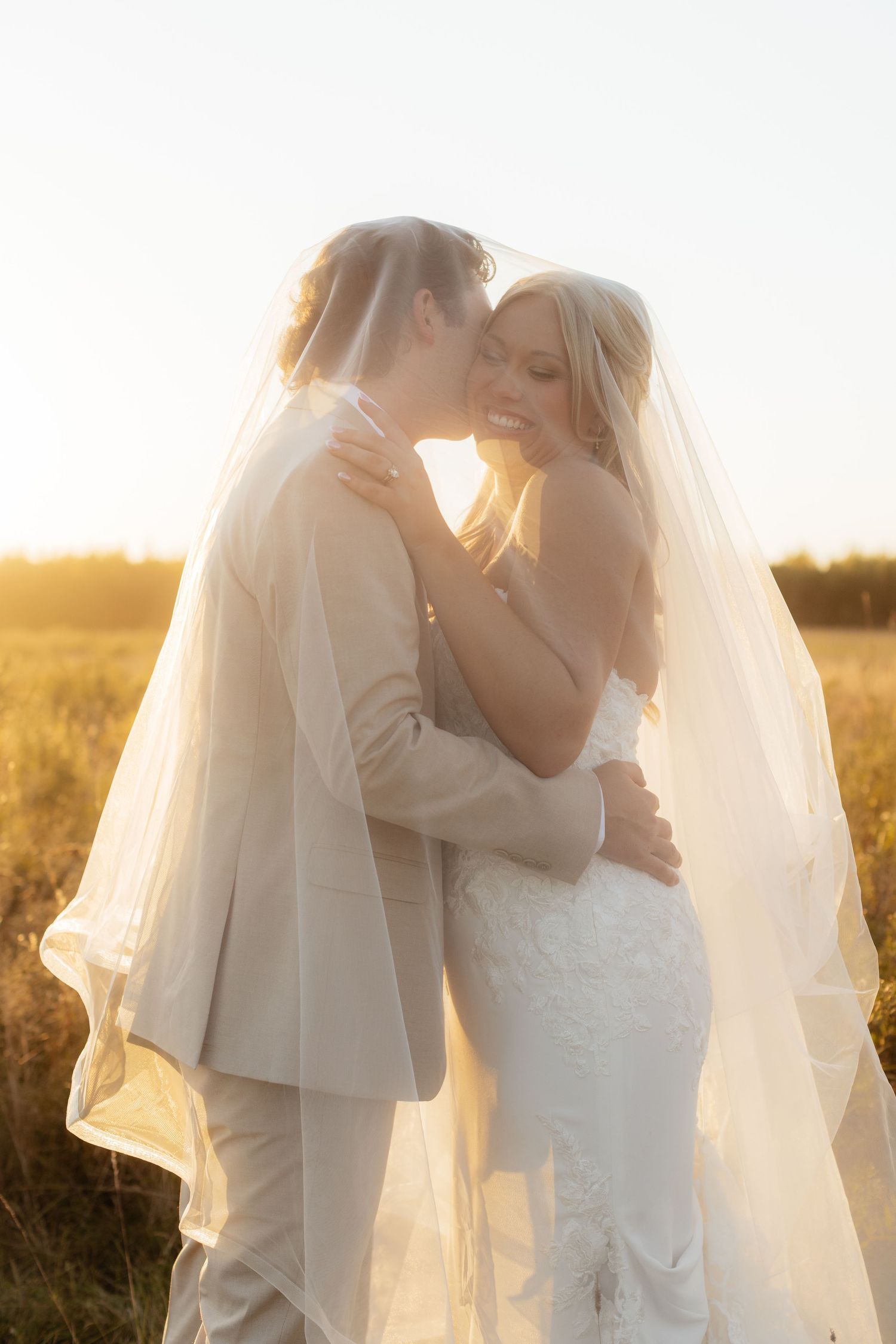 Wedding couple embracing in golden sunlight with bride wearing flowing veil.