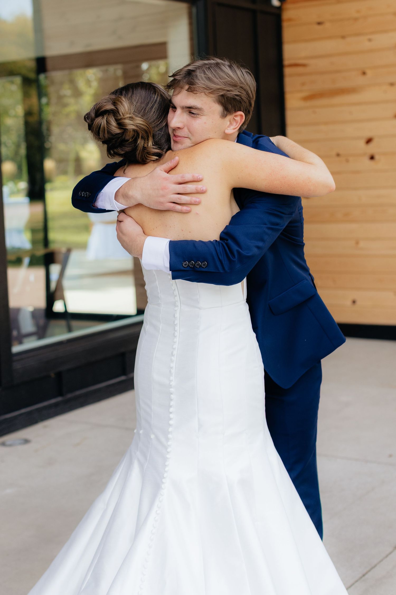 A tender moment between newlyweds outside a wooden-paneled building.