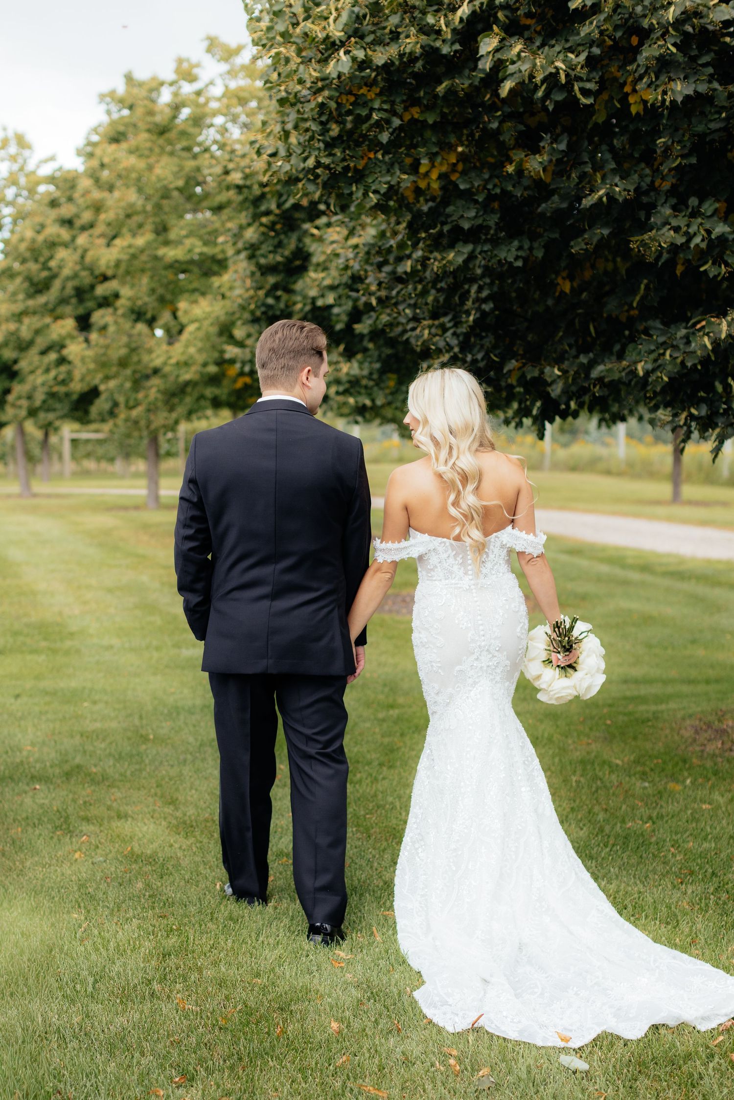 Wedding couple walking hand in hand across a lush green lawn on their special day.