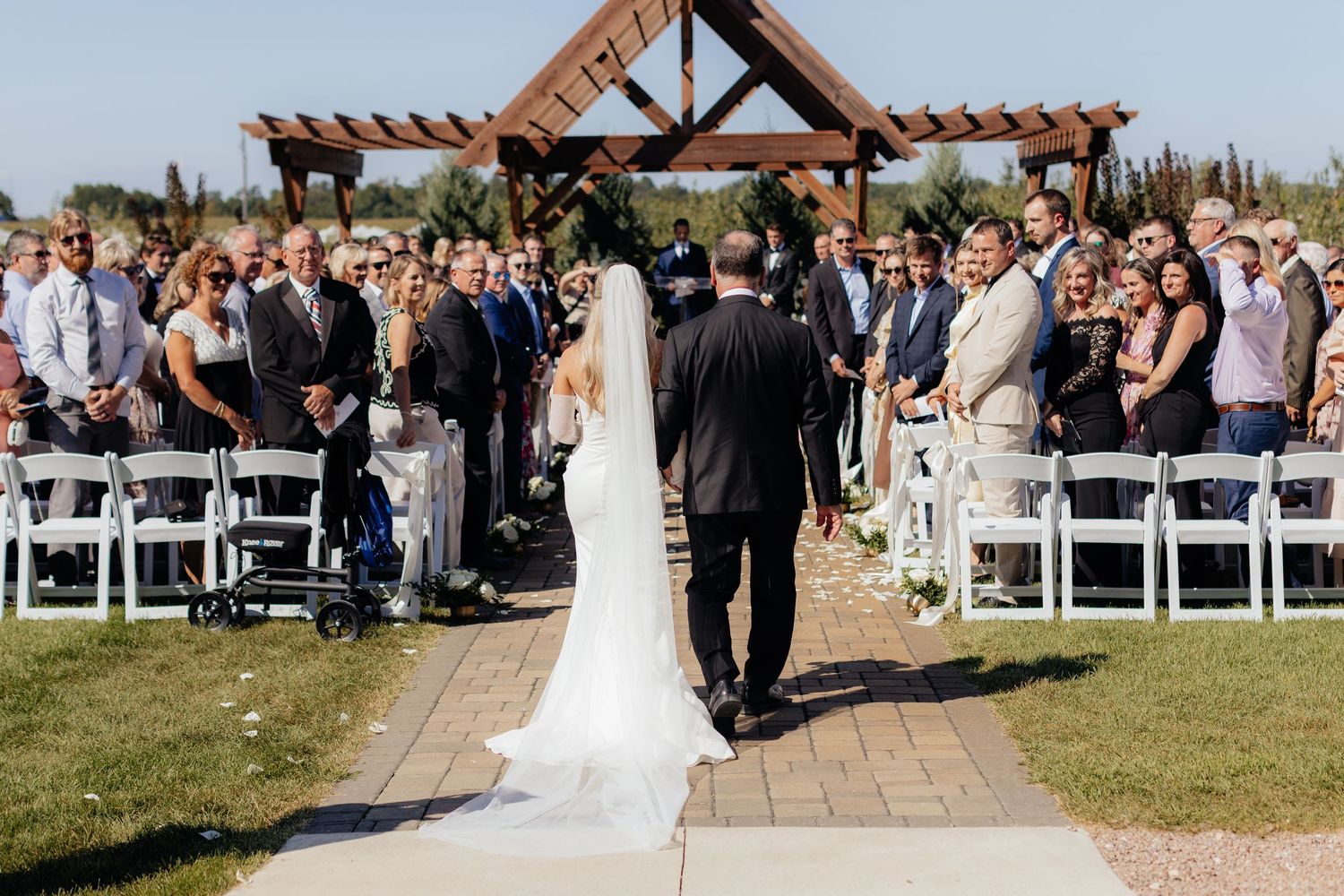 Newlyweds walking down aisle strewn with petals at outdoor venue.