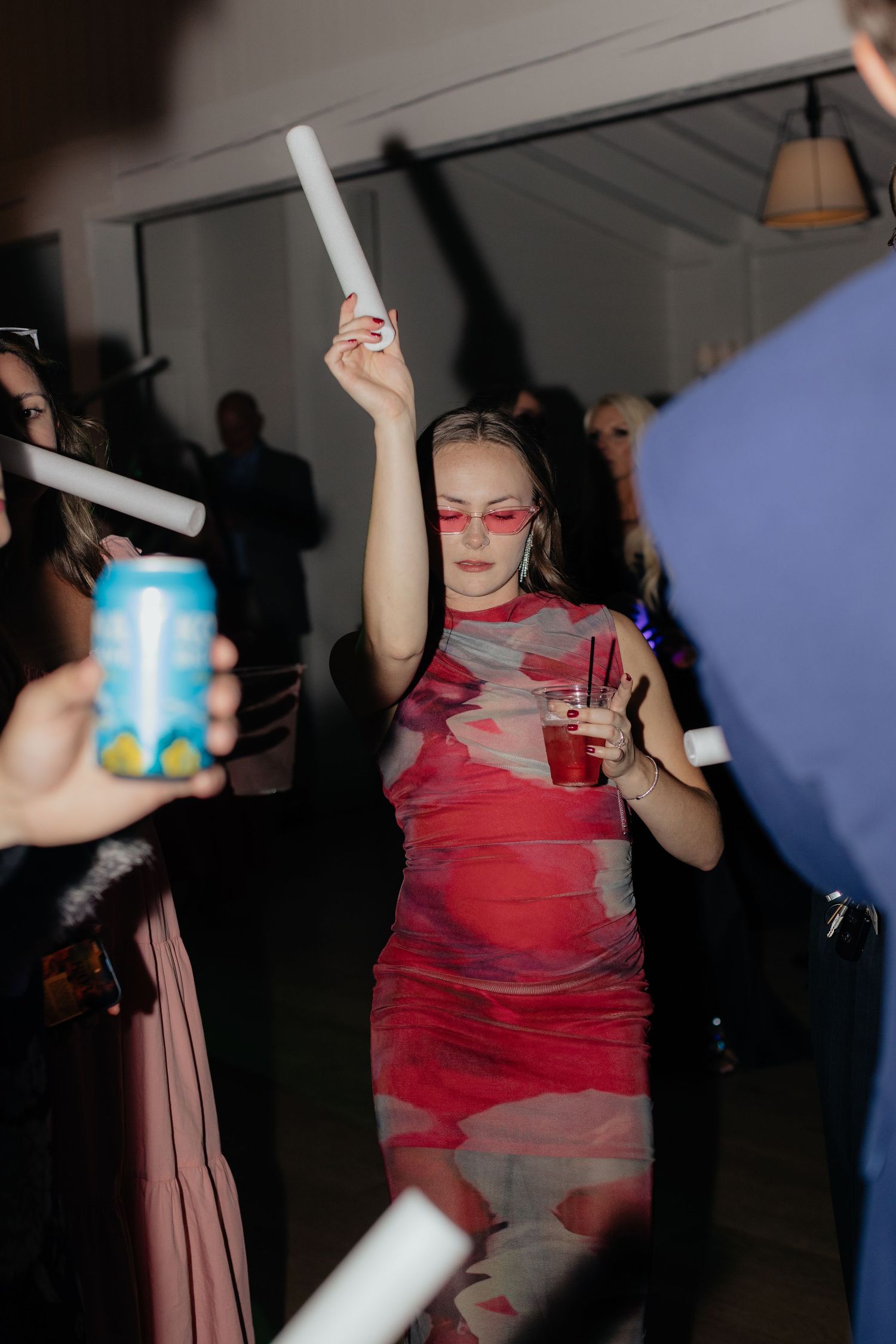 Wedding guest in red dress dancing with glowsticks at nighttime reception.