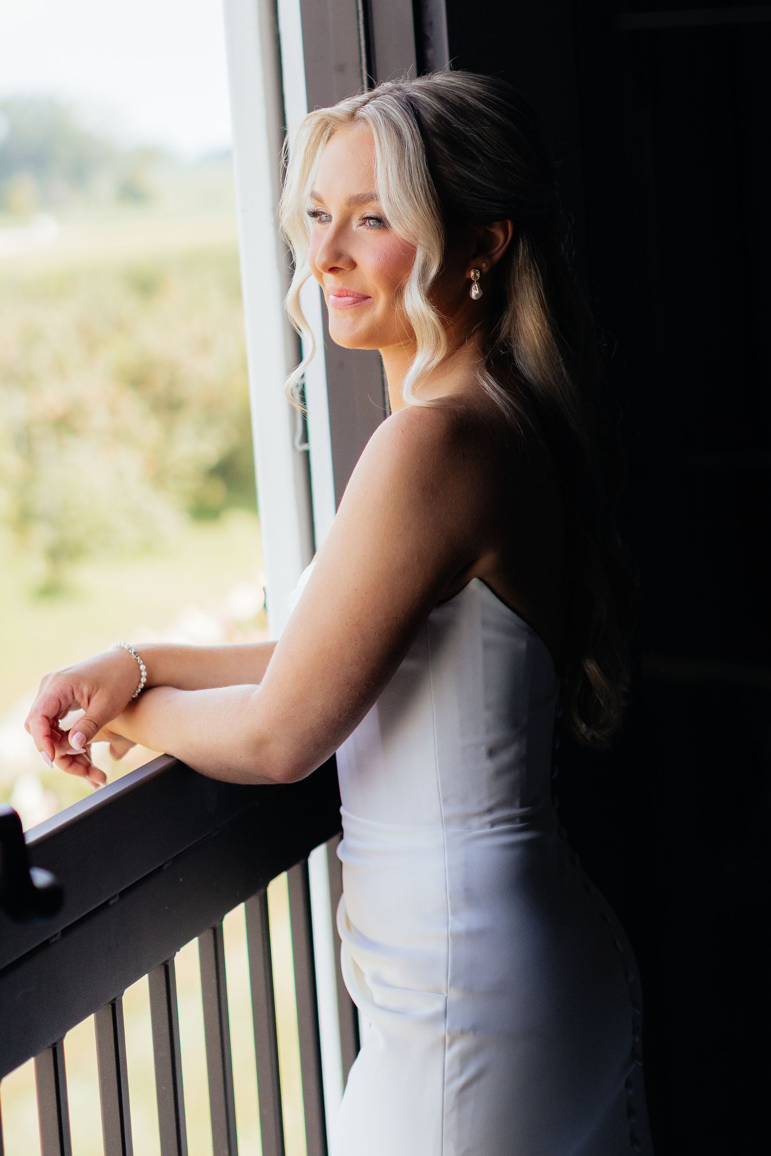 A bride in white gazing out a window during a quiet moment.