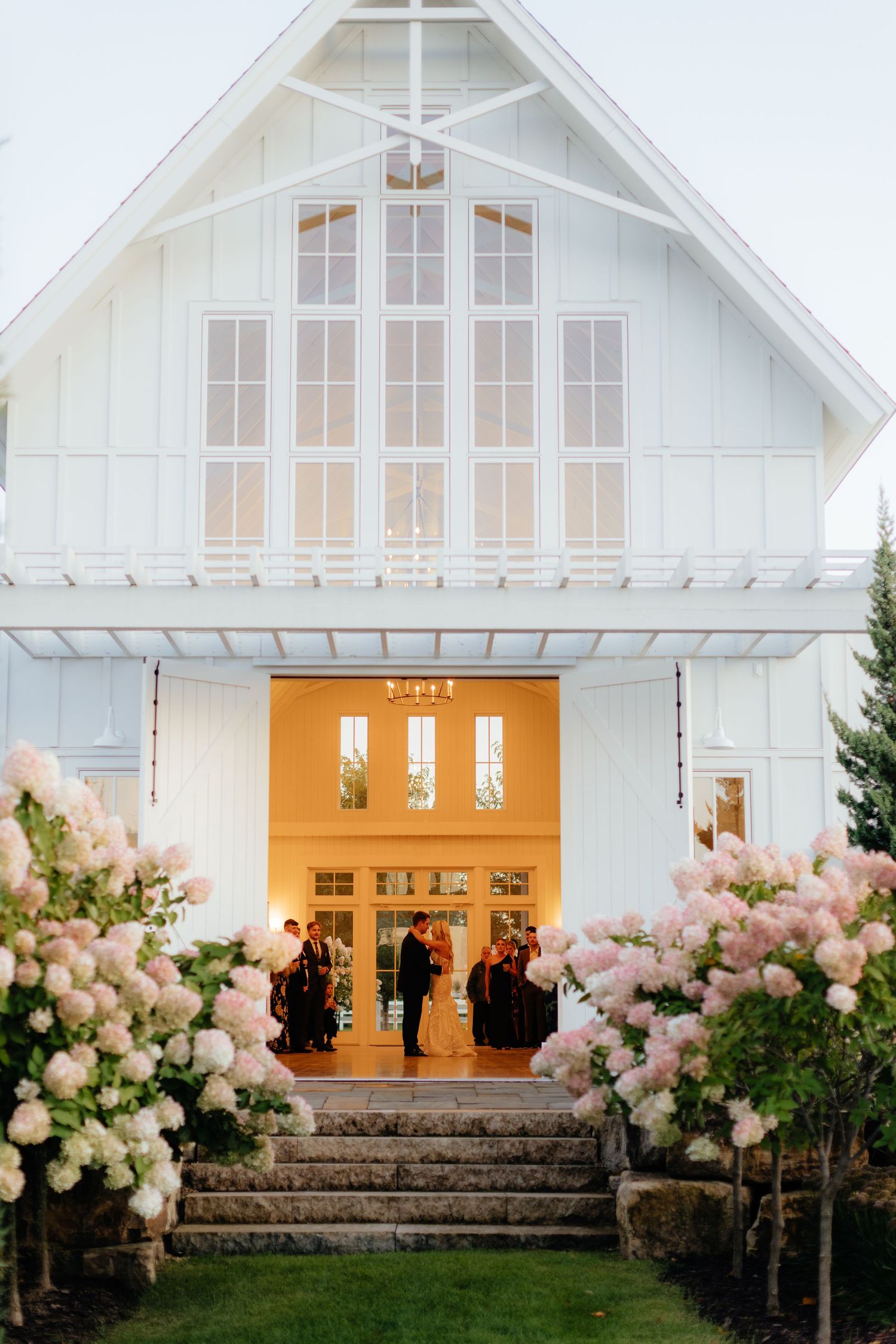 White chapel wedding venue with glowing windows and pink floral arrangements lining the entrance steps.