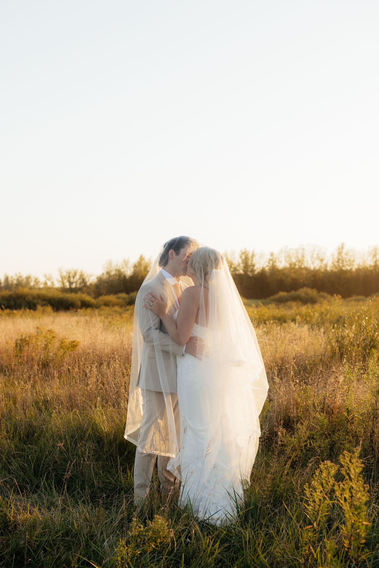 Wedding couple standing together in tall grass during golden hour photography session.