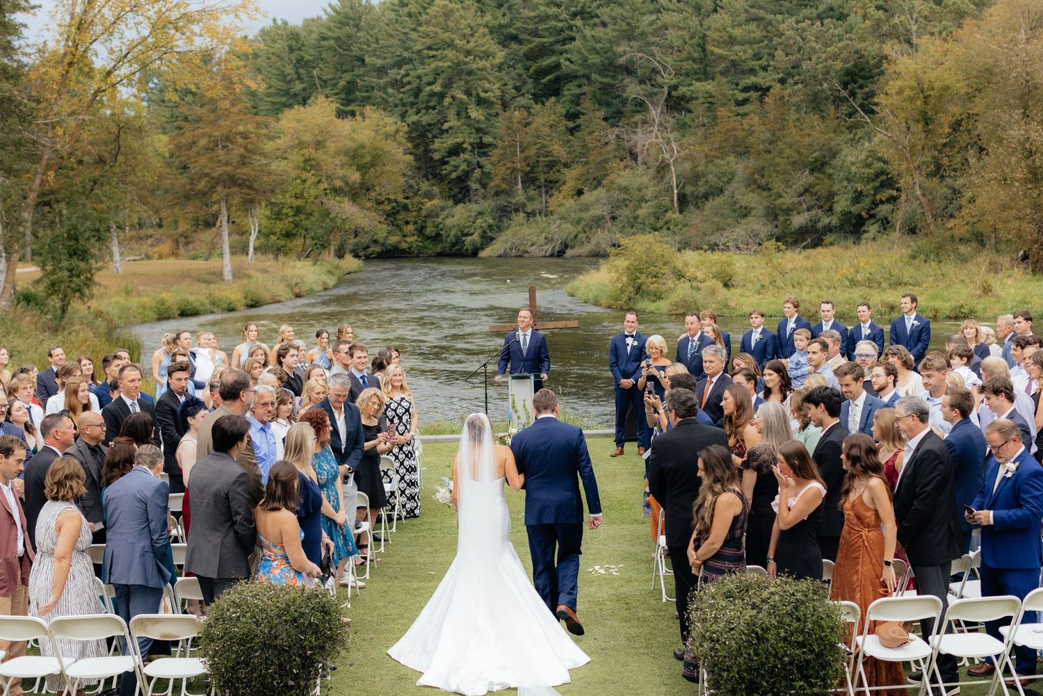 Outdoor wedding ceremony setup with white chairs and natural forest scenery.