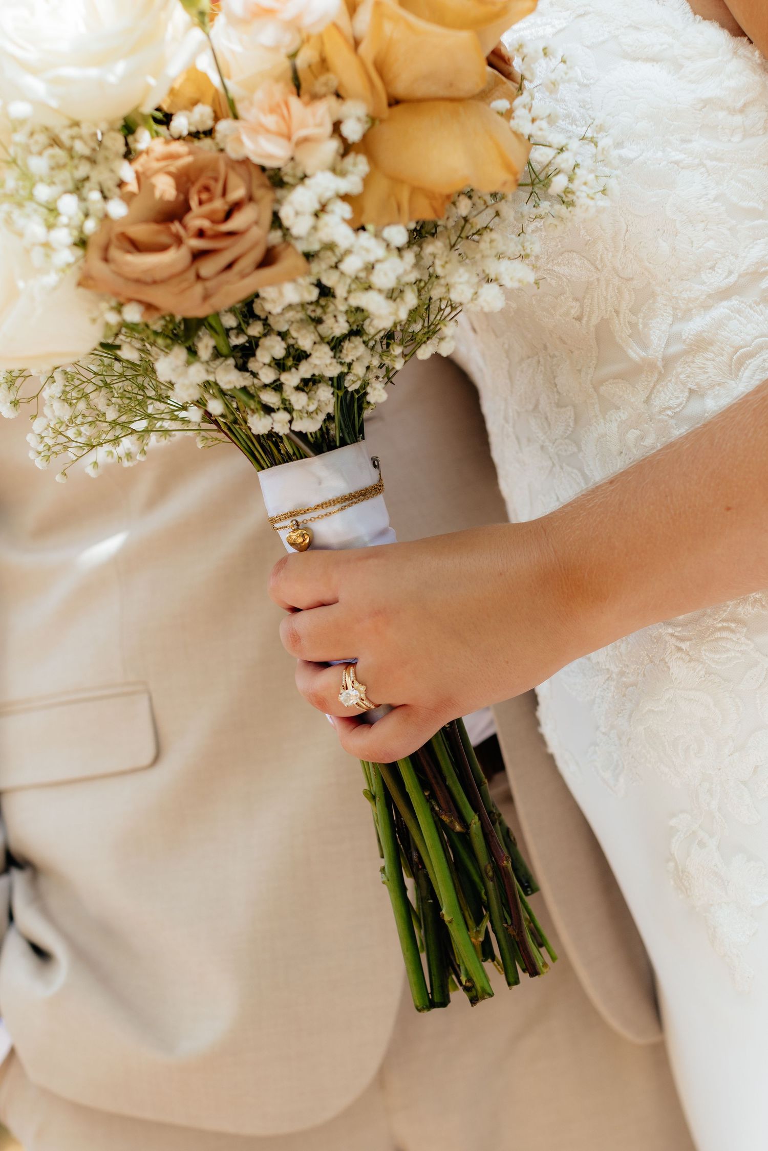Close-up of a bridal bouquet with peach roses and baby's breath flowers against a white wedding dress.