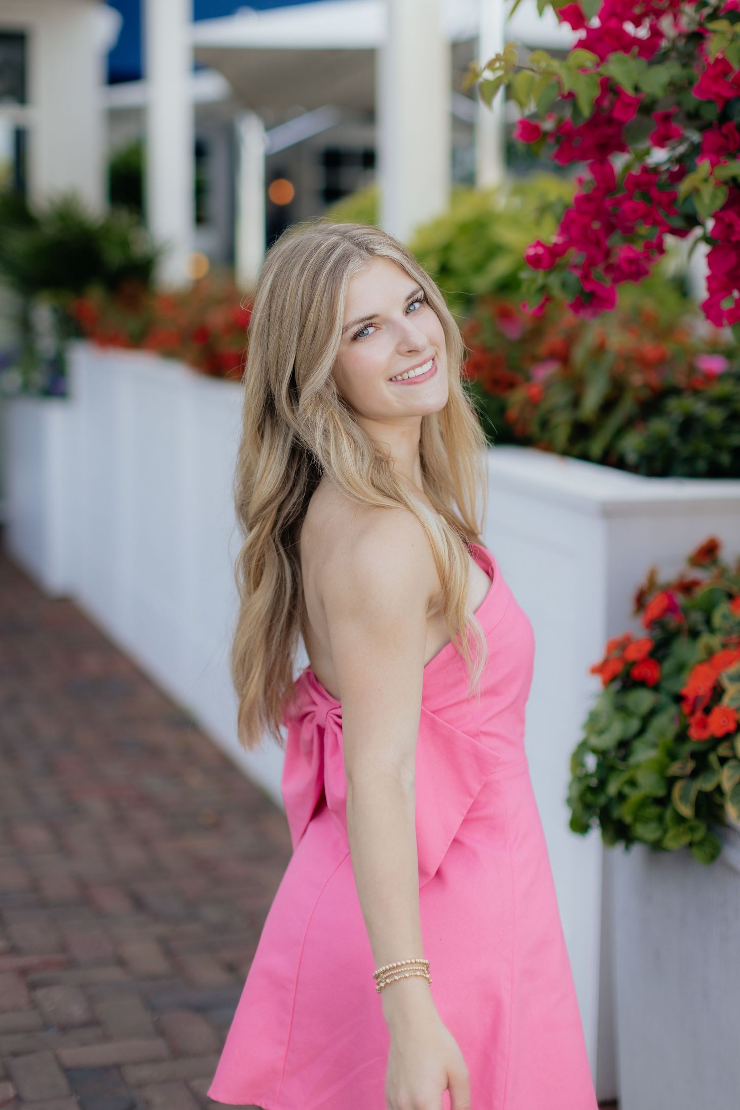 A pink sundress is showcased against vibrant red flowers and white architectural details.