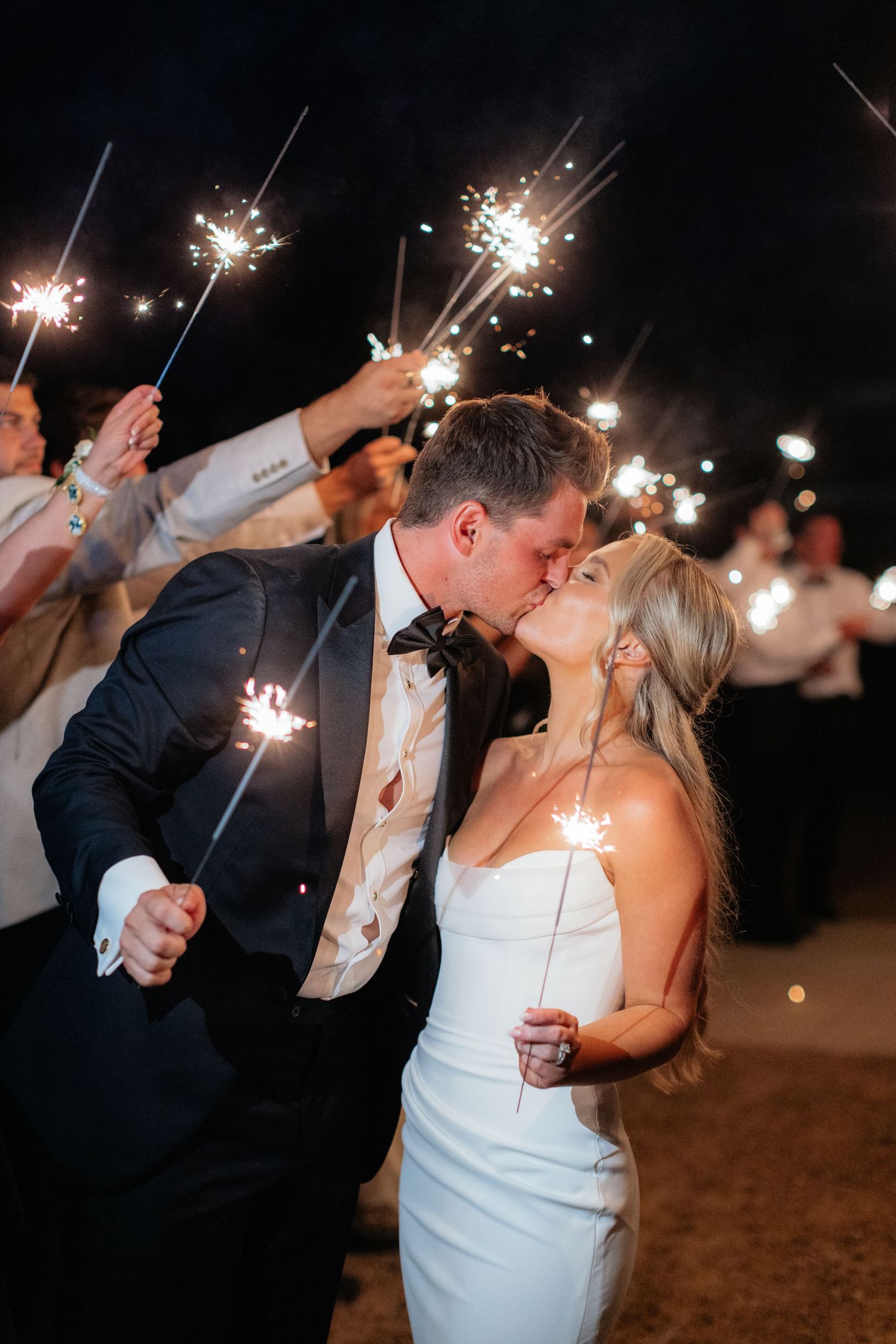 Couple shares intimate moment during sparkler send-off at nighttime wedding celebration.