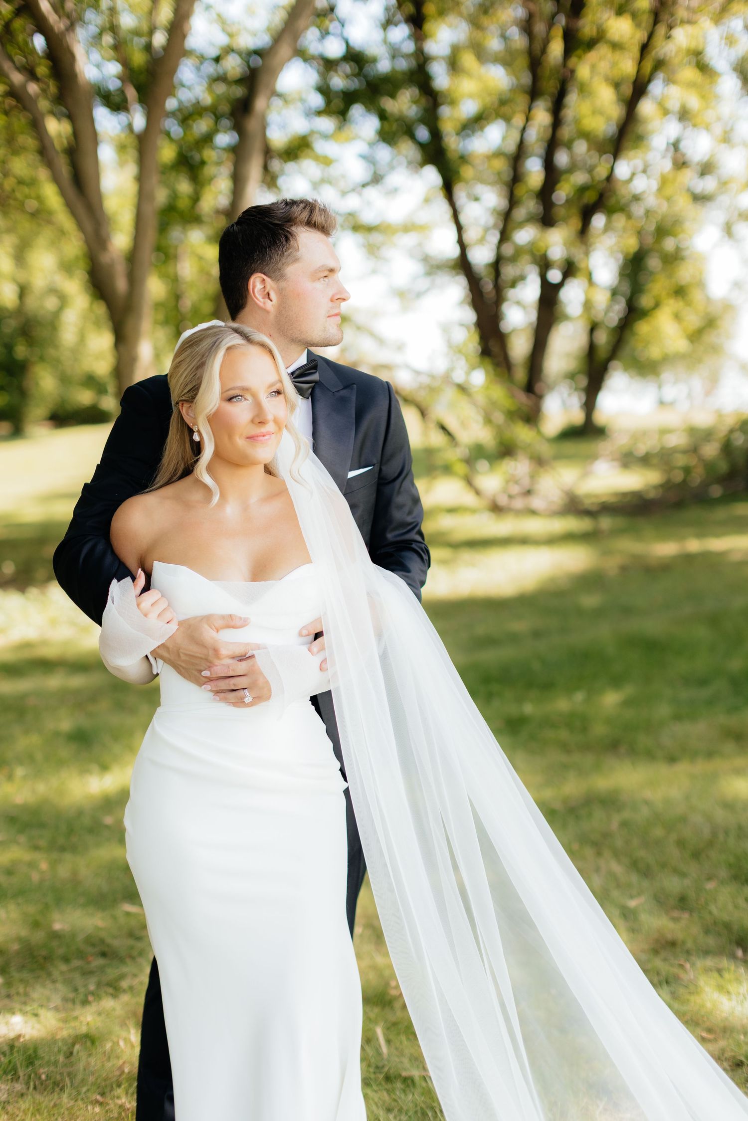 Sun-drenched wedding photos with couple embracing on grassy hillside.