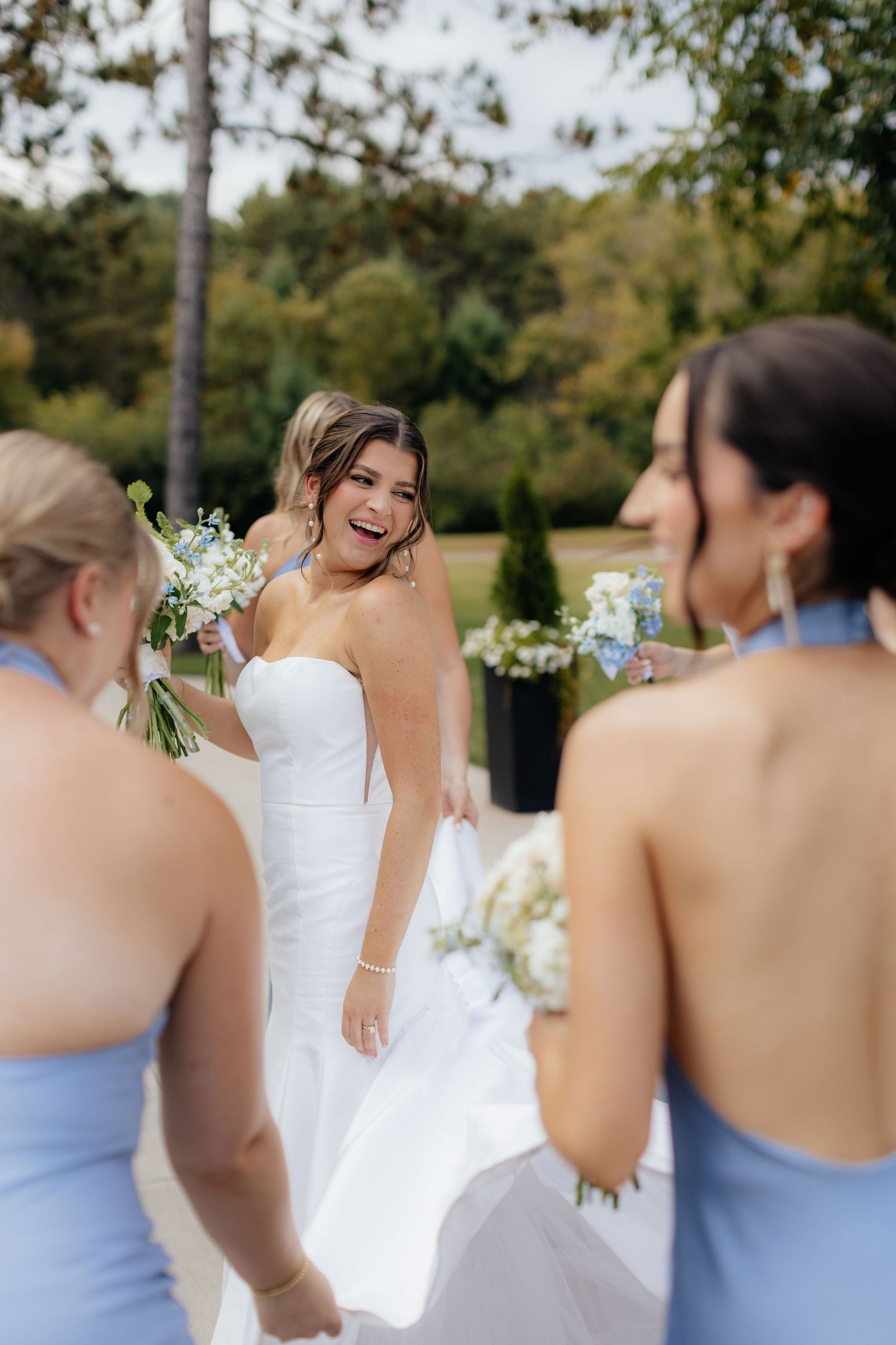 Bridesmaids in light blue dresses share a joyful moment with the bride in a white gown during an outdoor celebration.