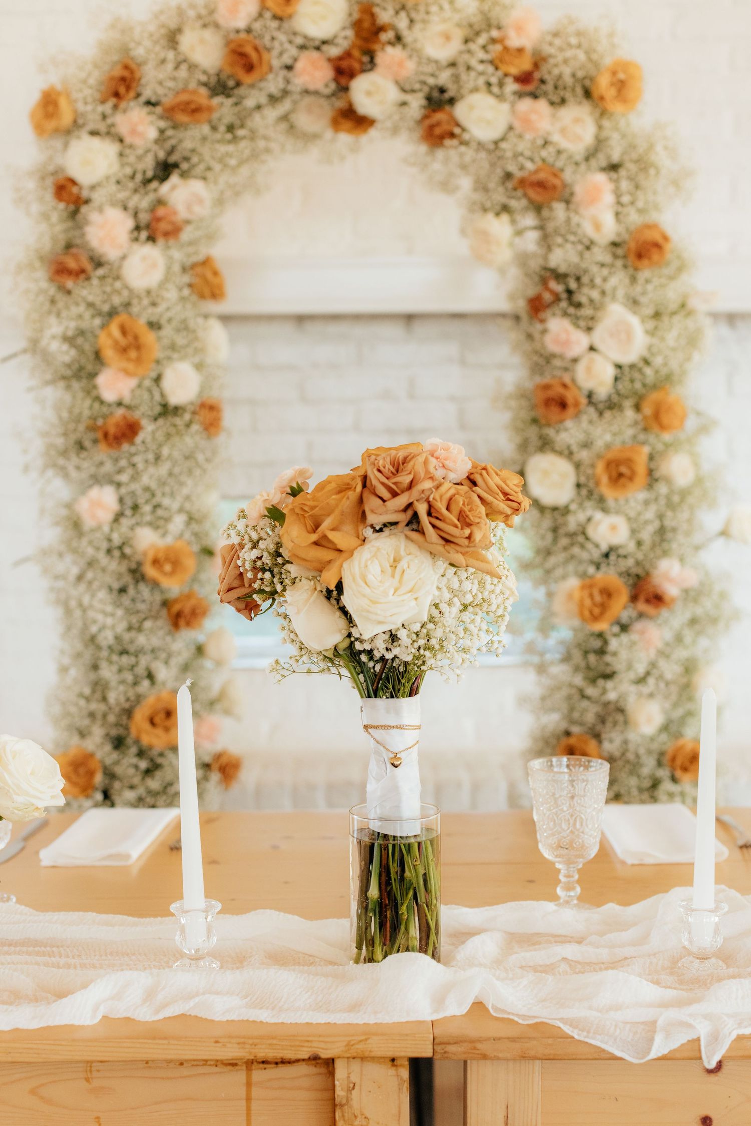 Elegant table setting with peach and cream floral arrangements and white candles against a floral backdrop.