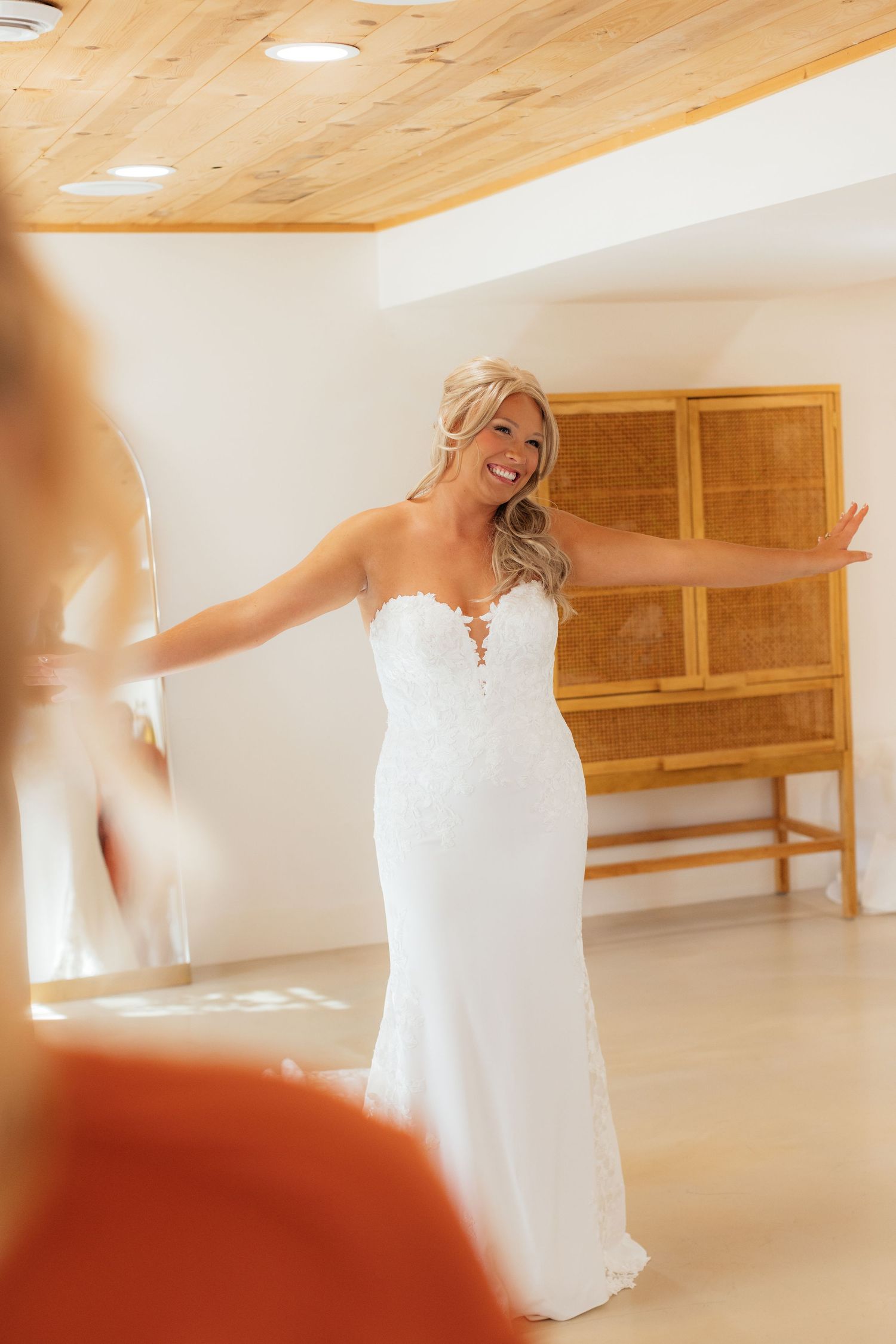Bride in lace wedding dress twirling in bright room with wooden ceiling.