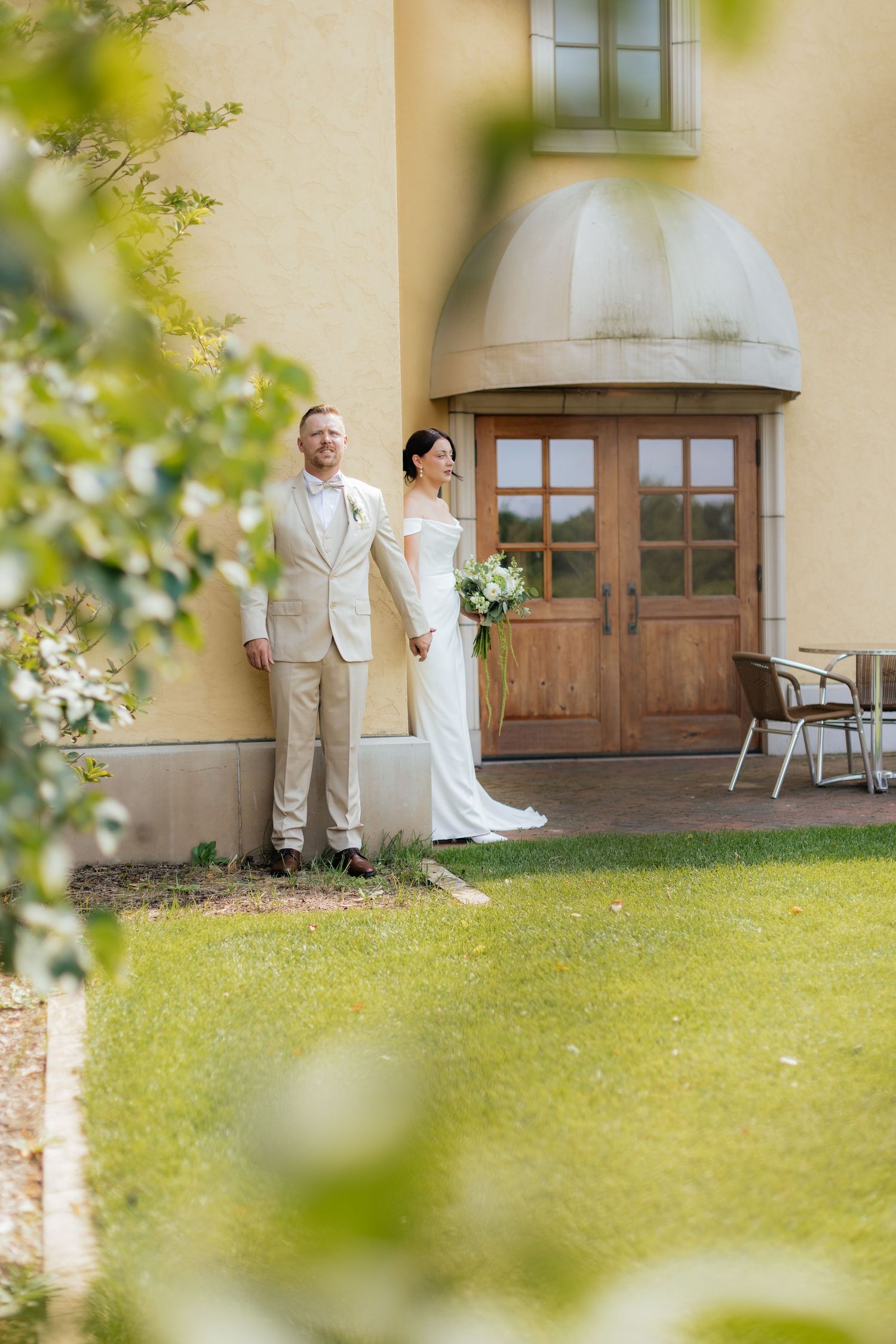 Artistic wedding photos captured through foliage showing couple against yellow building exterior.