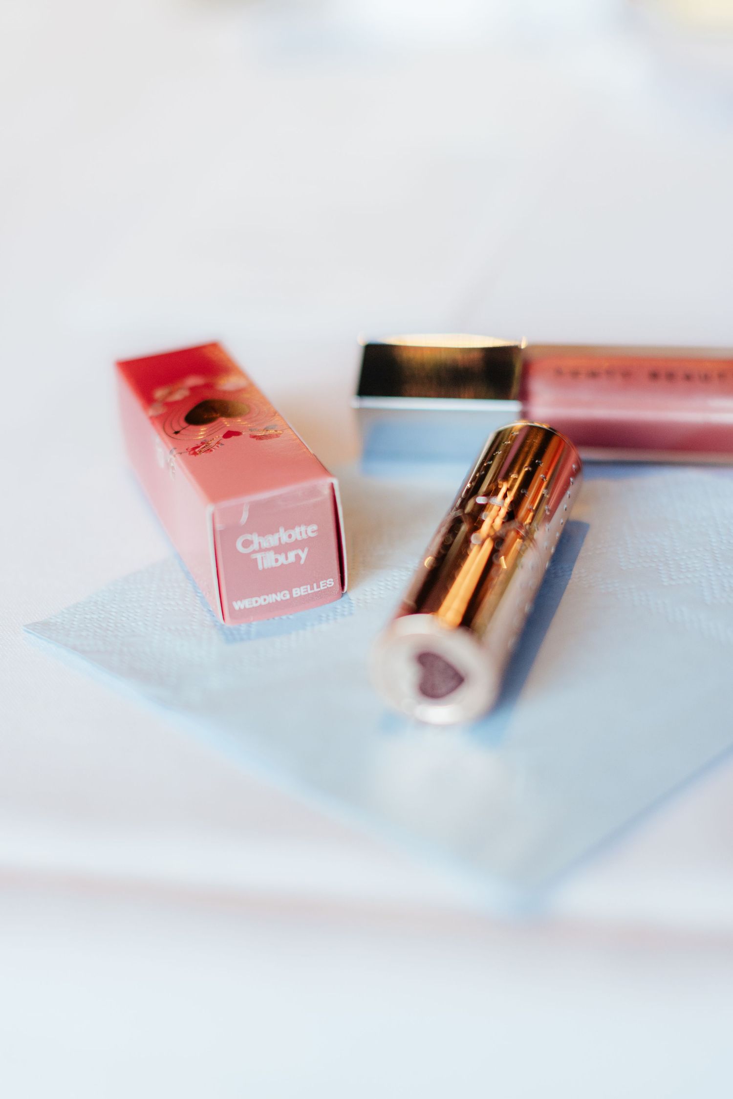 Pink and rose gold cosmetic products arranged on light blue surface.