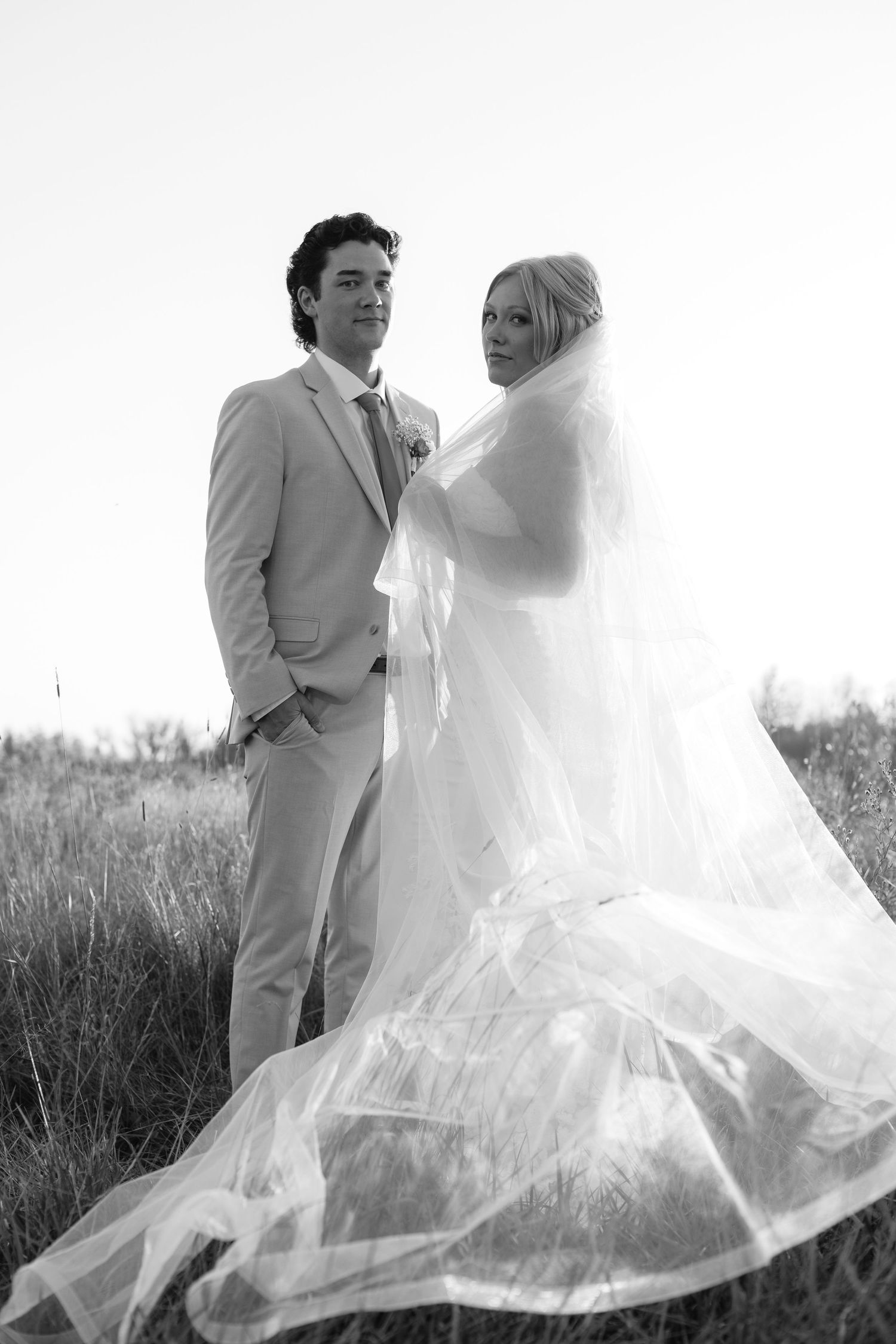 Black and white portrait of newlyweds with flowing veil in natural setting.