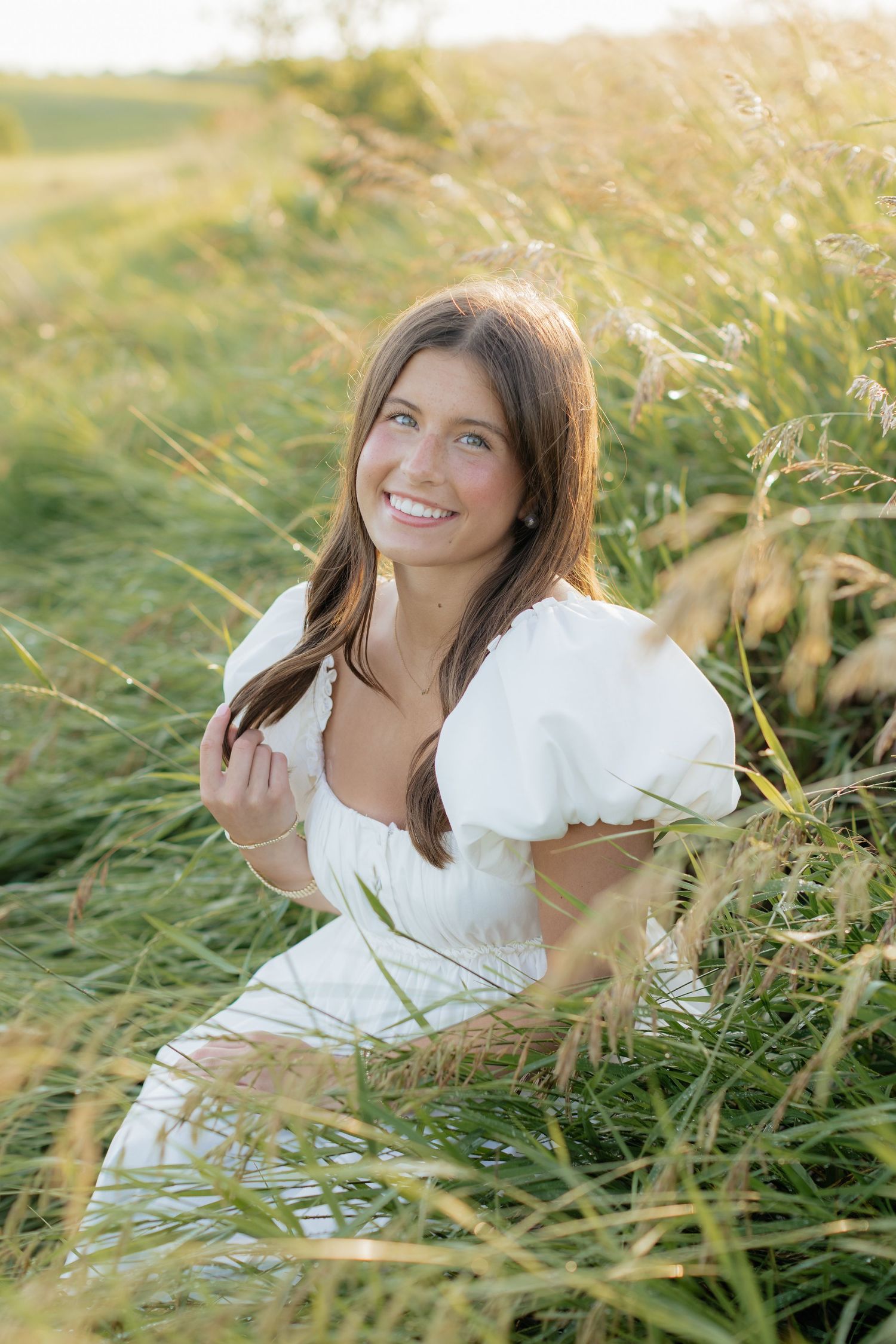 A white summer dress with puff sleeves is photographed in a sunlit field of tall grass.