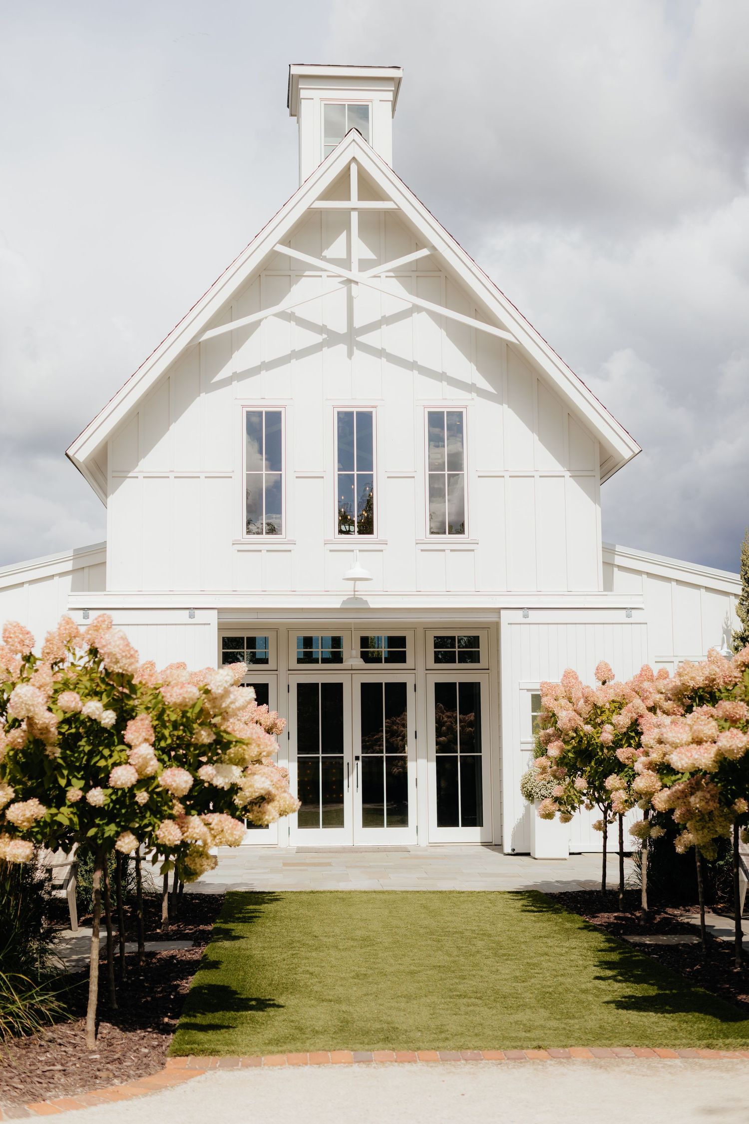 White farmhouse style wedding venue with blooming pink hydrangea bushes along the facade.