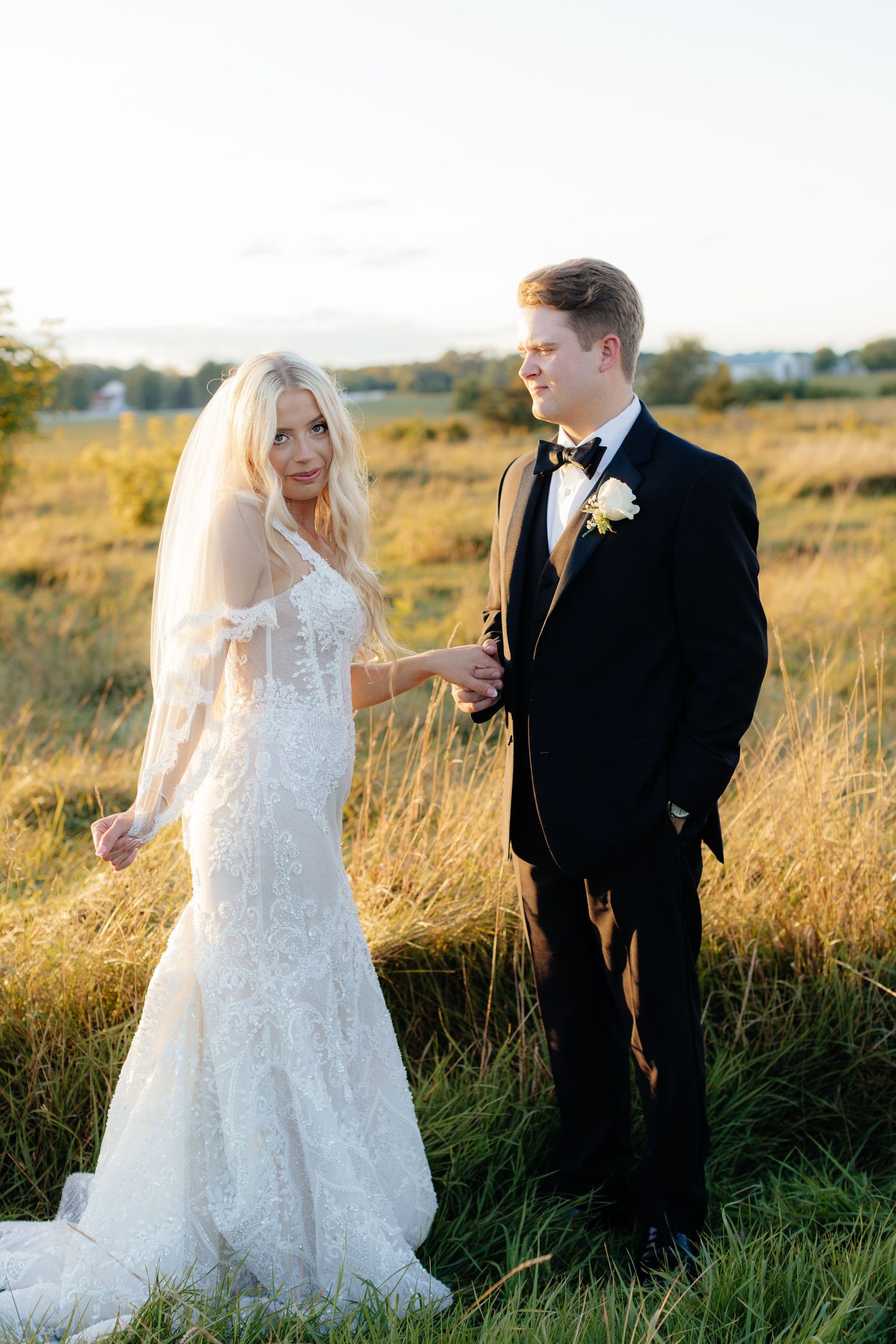 Newlyweds share candid moments while walking through tall grass at sunset.