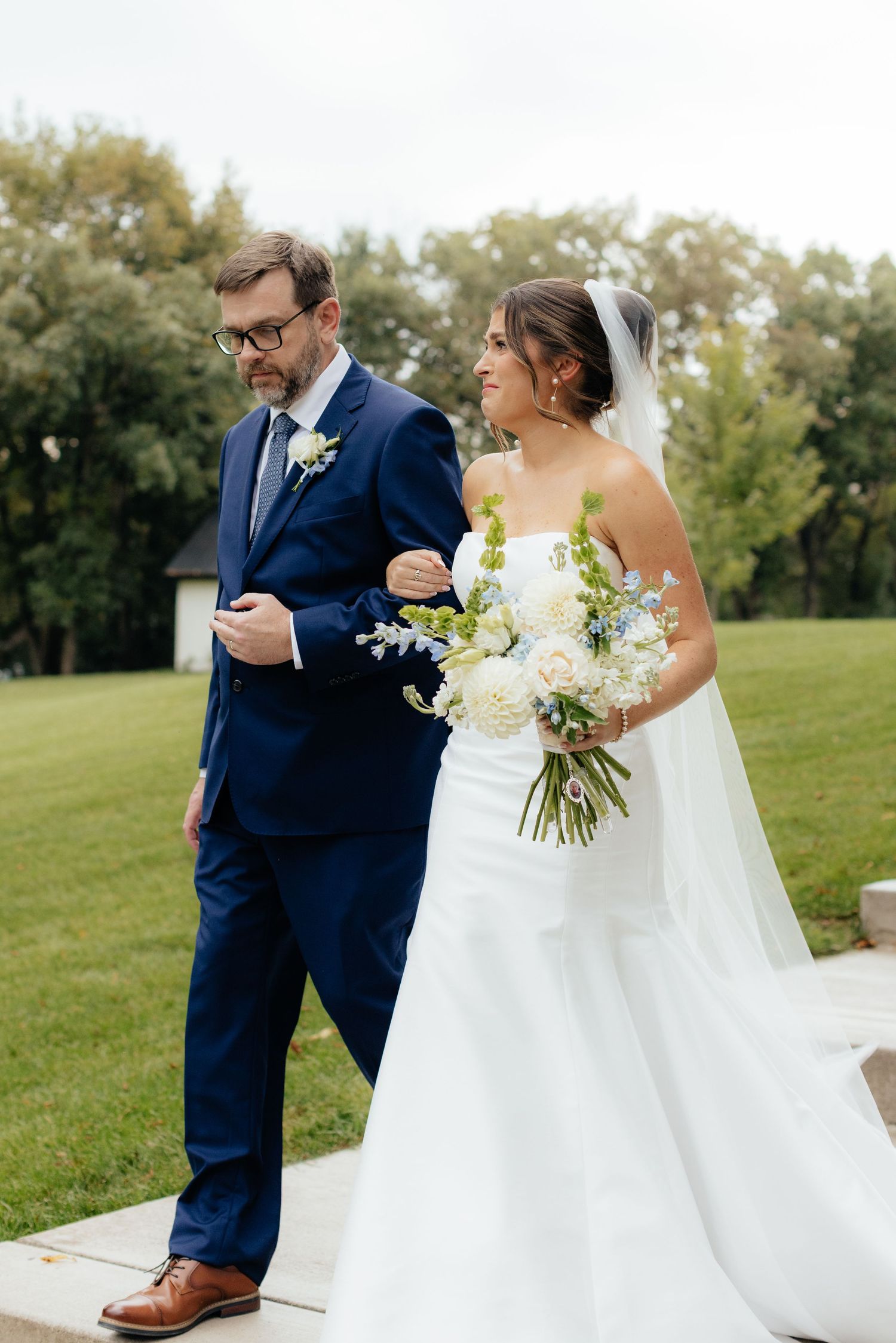 Wedding couple walking together on lush green lawn during outdoor celebration.