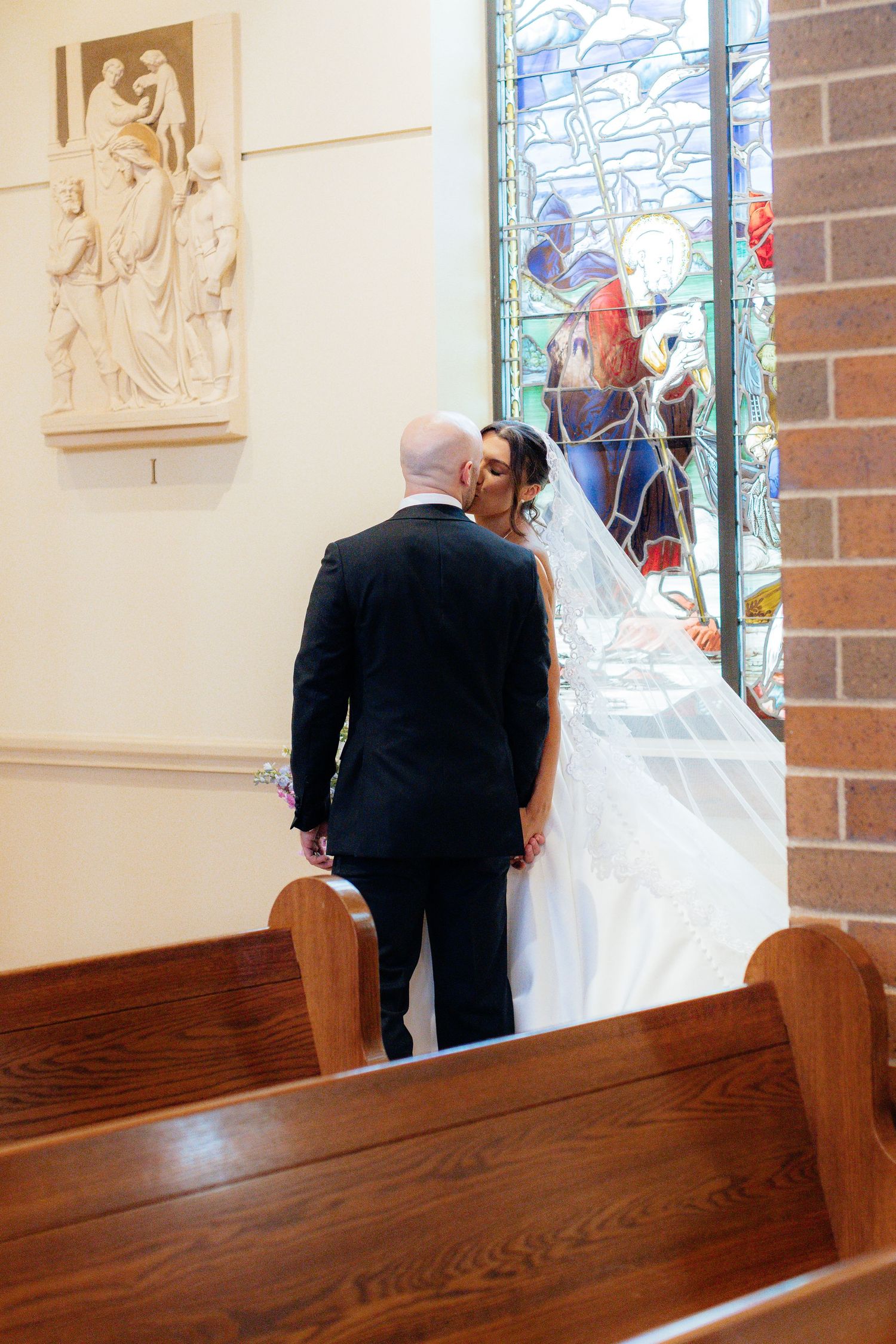 A church interior with wooden pews and stained glass windows during a wedding ceremony.