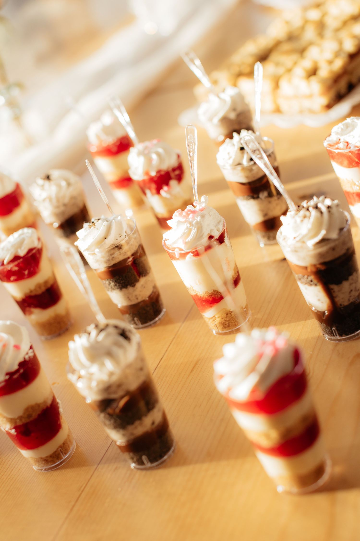 Row of layered dessert parfaits with cream and red filling in small glass containers.
