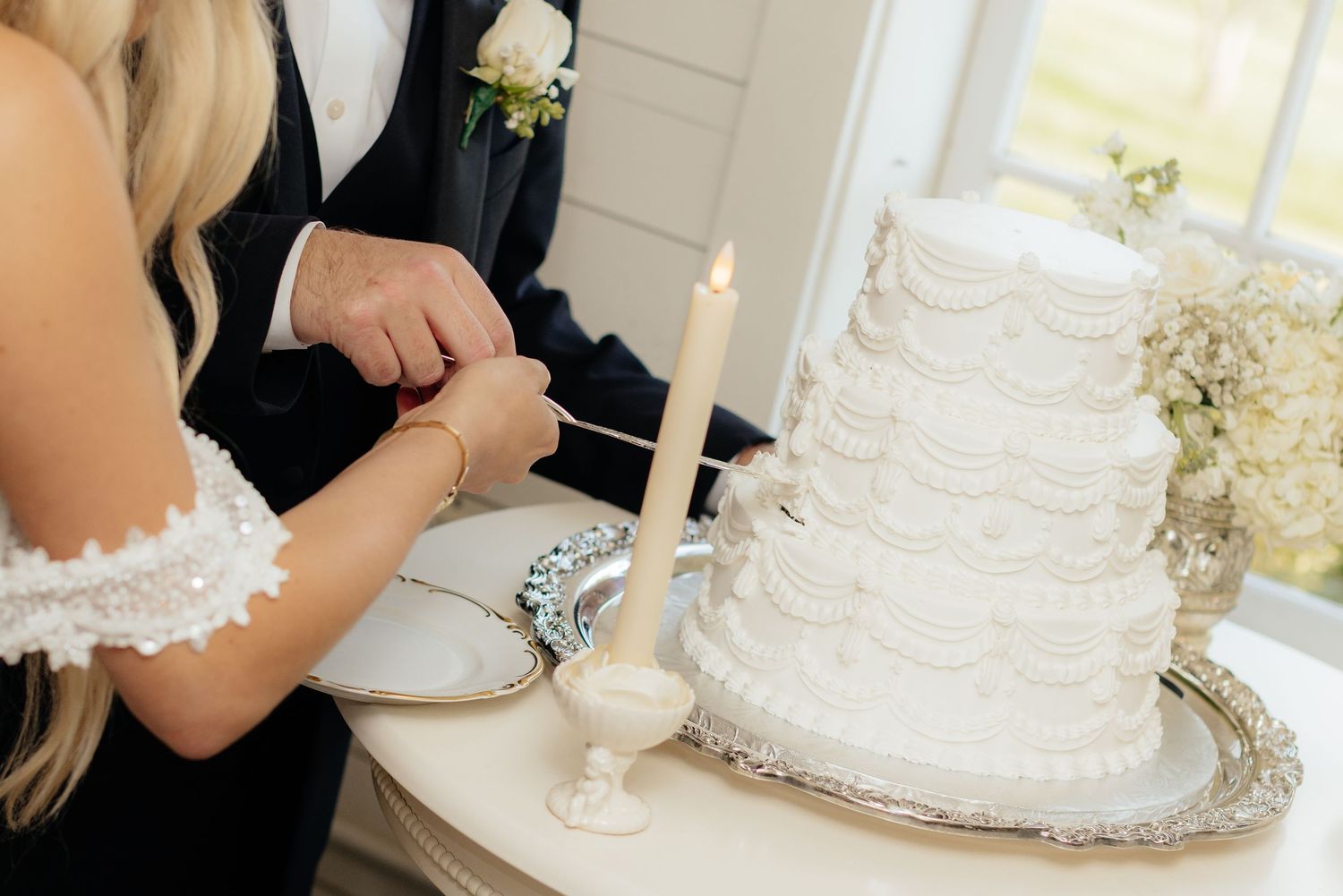 Elegant white wedding cake with intricate piping details displayed on a silver tray.