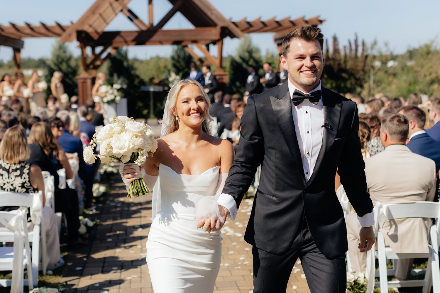 A joyful wedding ceremony exit under a rustic wooden pergola.